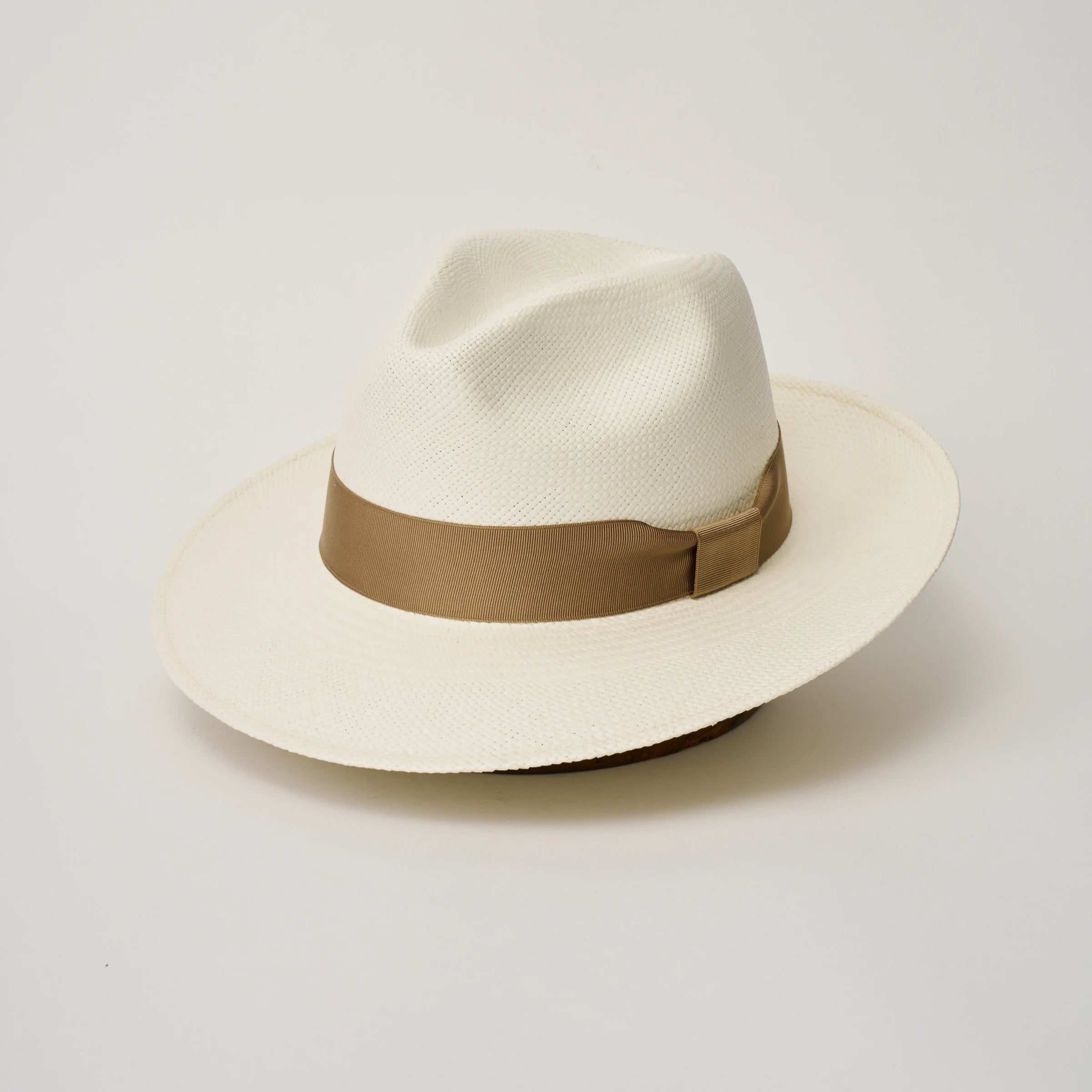 Studio image, angle view of the Camilo Classic Cream coloured Panama Hat with Tan trim, showing the crown shape, front crease and ribbon finish.