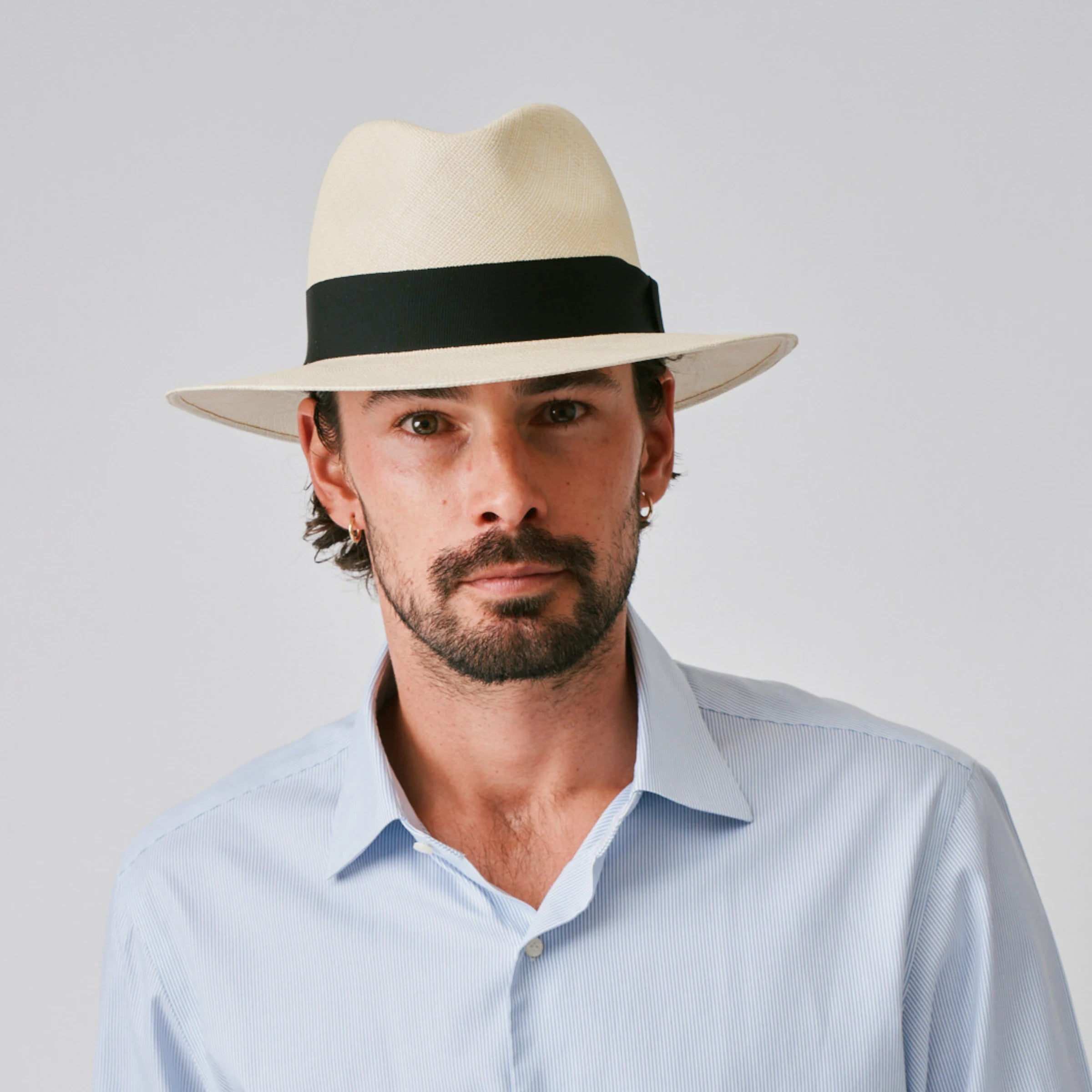 Man wearing a Executive Fino Natural / Black Panama hat and blue shirt against a plain background.