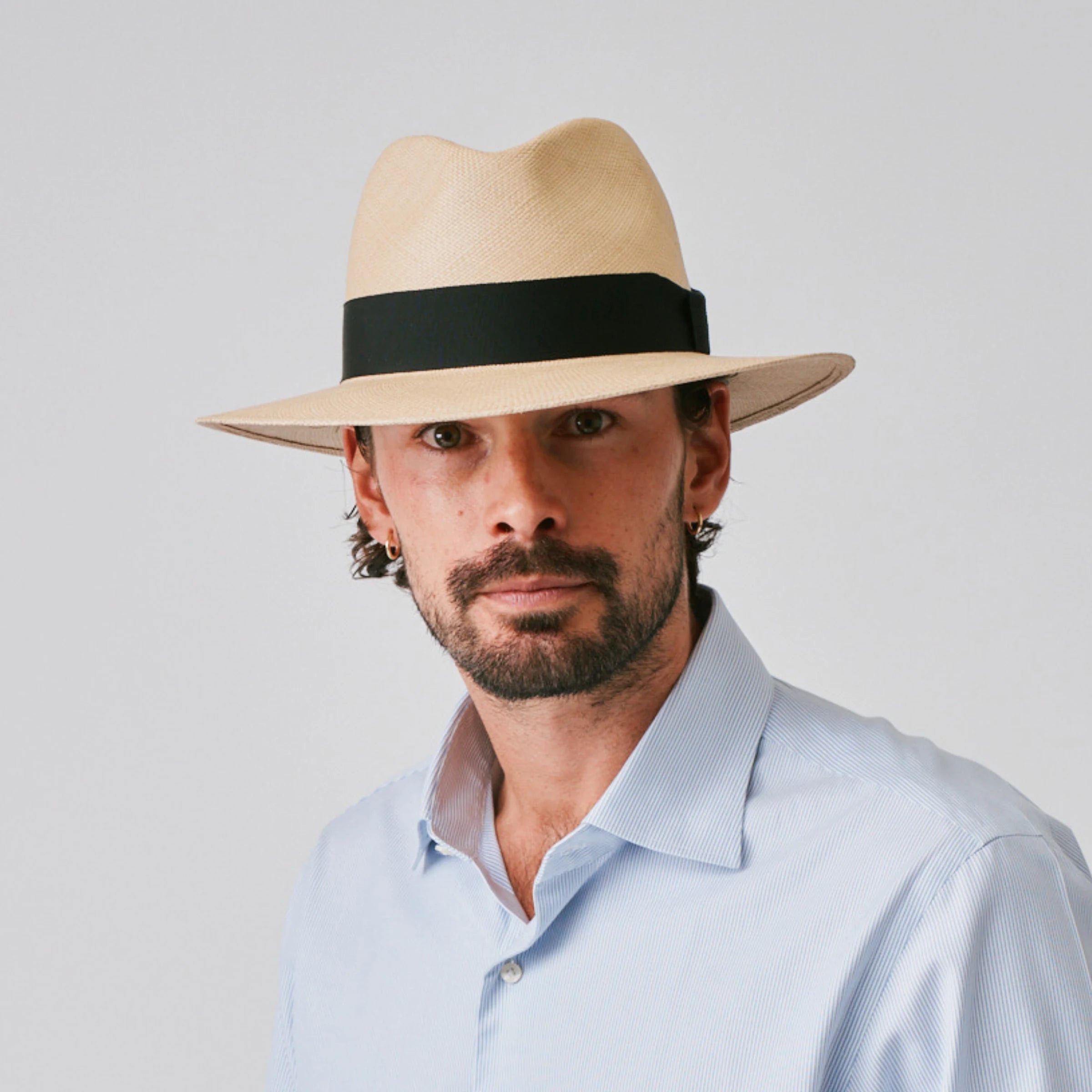 Man wearing a Executive Fino Sand / Black Panama hat and blue shirt against a plain background.