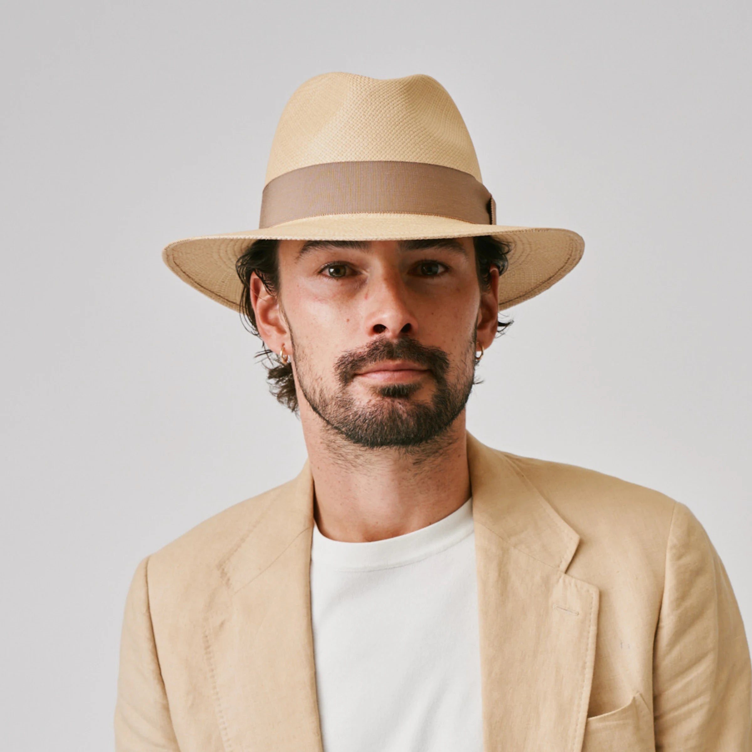 Man wearing a Executive Sand / Oat Panama hat and linen jacket against a plain background.
