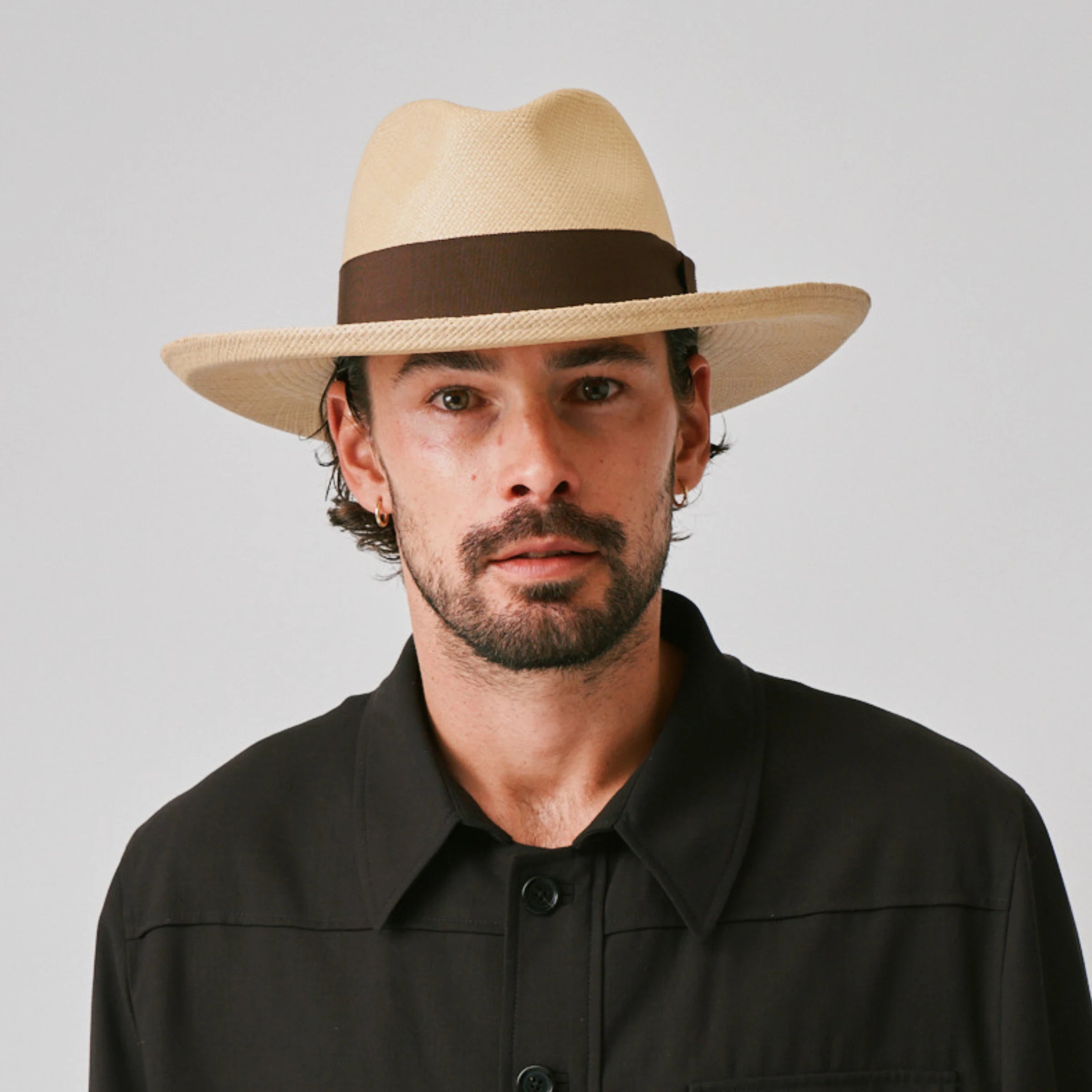 Man wearing a Grand Planter Sand / Chocolate Panama hat and black shirt against a plain background.