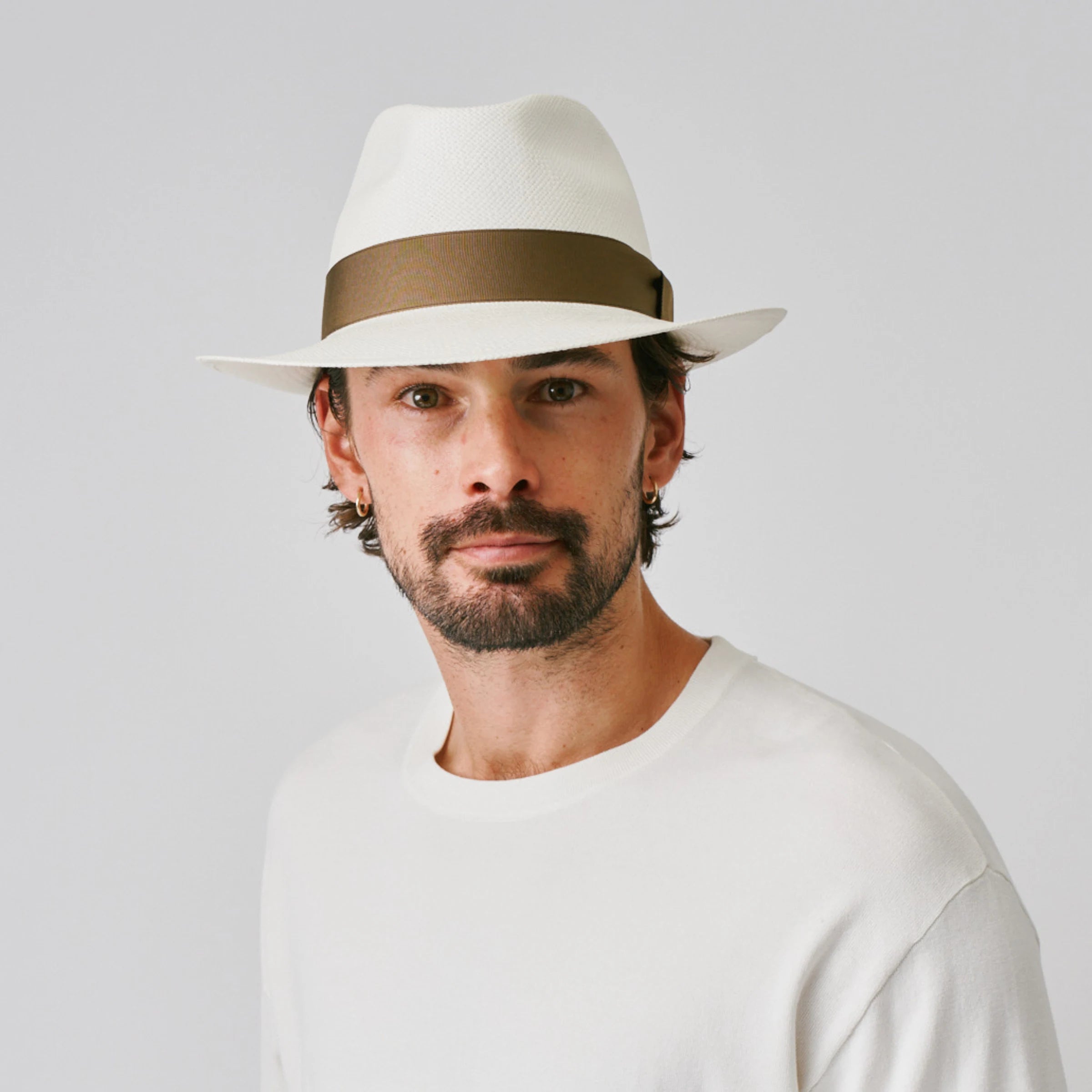 Man wearing a New Fedora Cream / Fawn Panama hat and white top against a plain background.