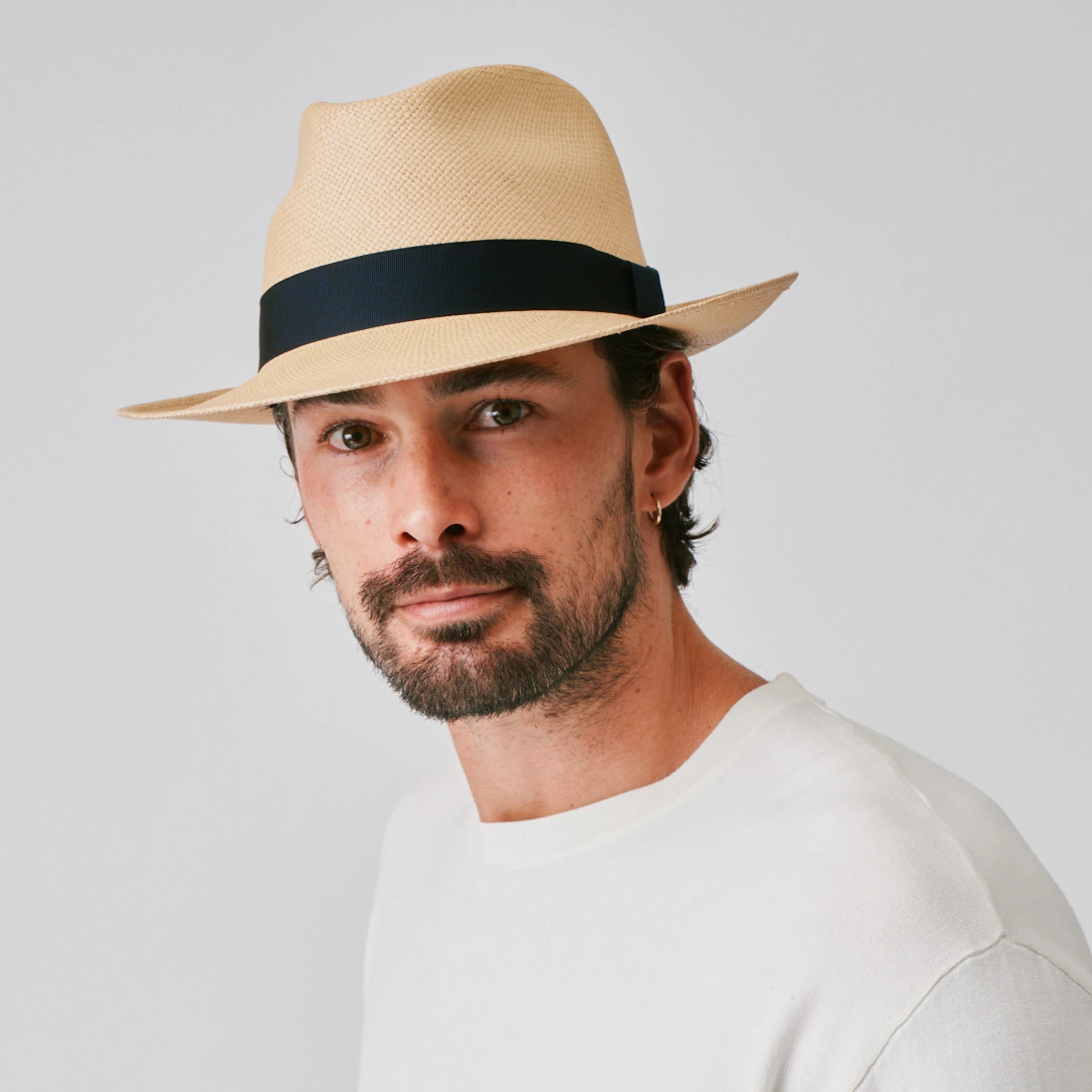 Man wearing a New Fedora Sand / Marine Panama hat and white top against a plain background.