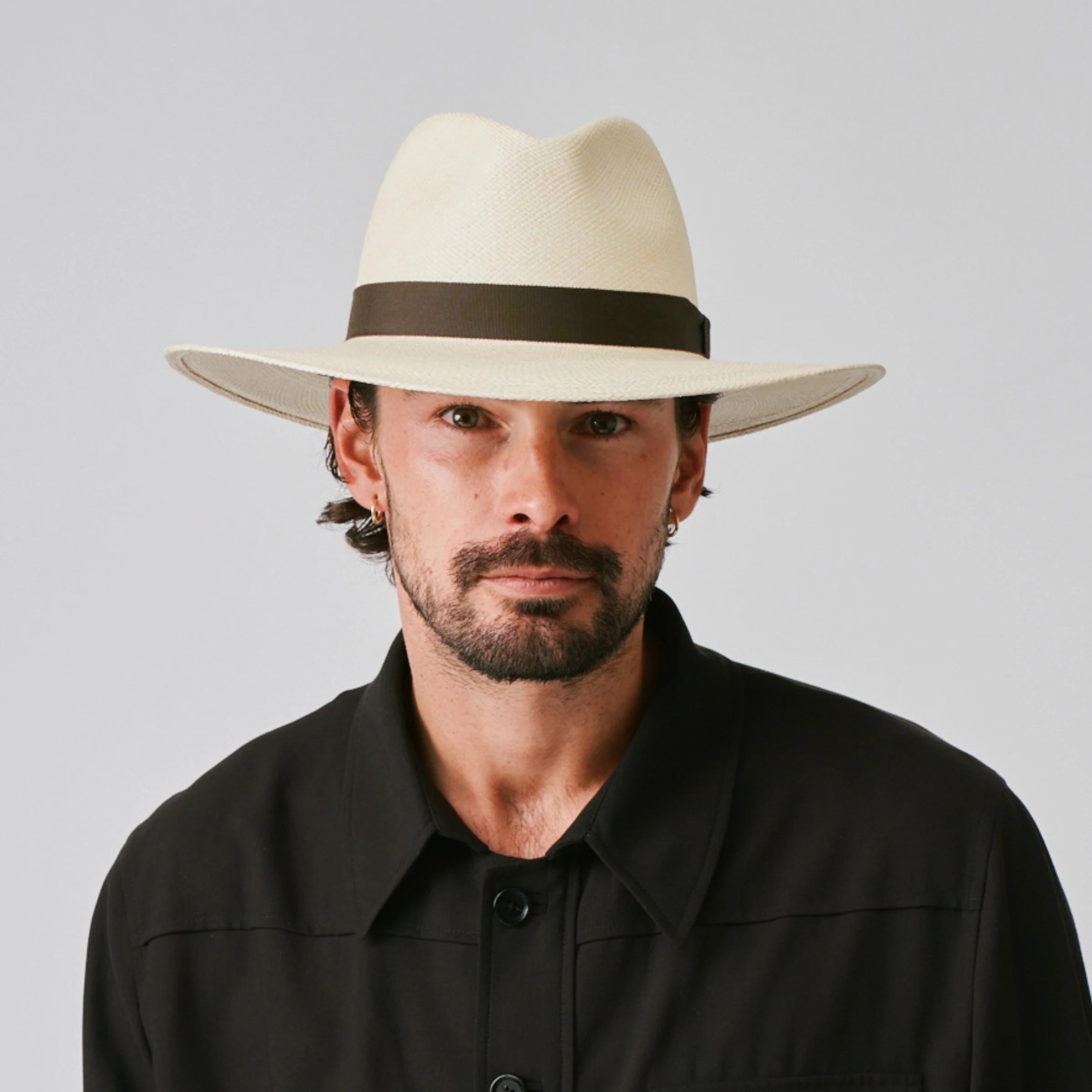 Man wearing a Oro Natural / Espresso Panama hat and black shirt against a plain background.