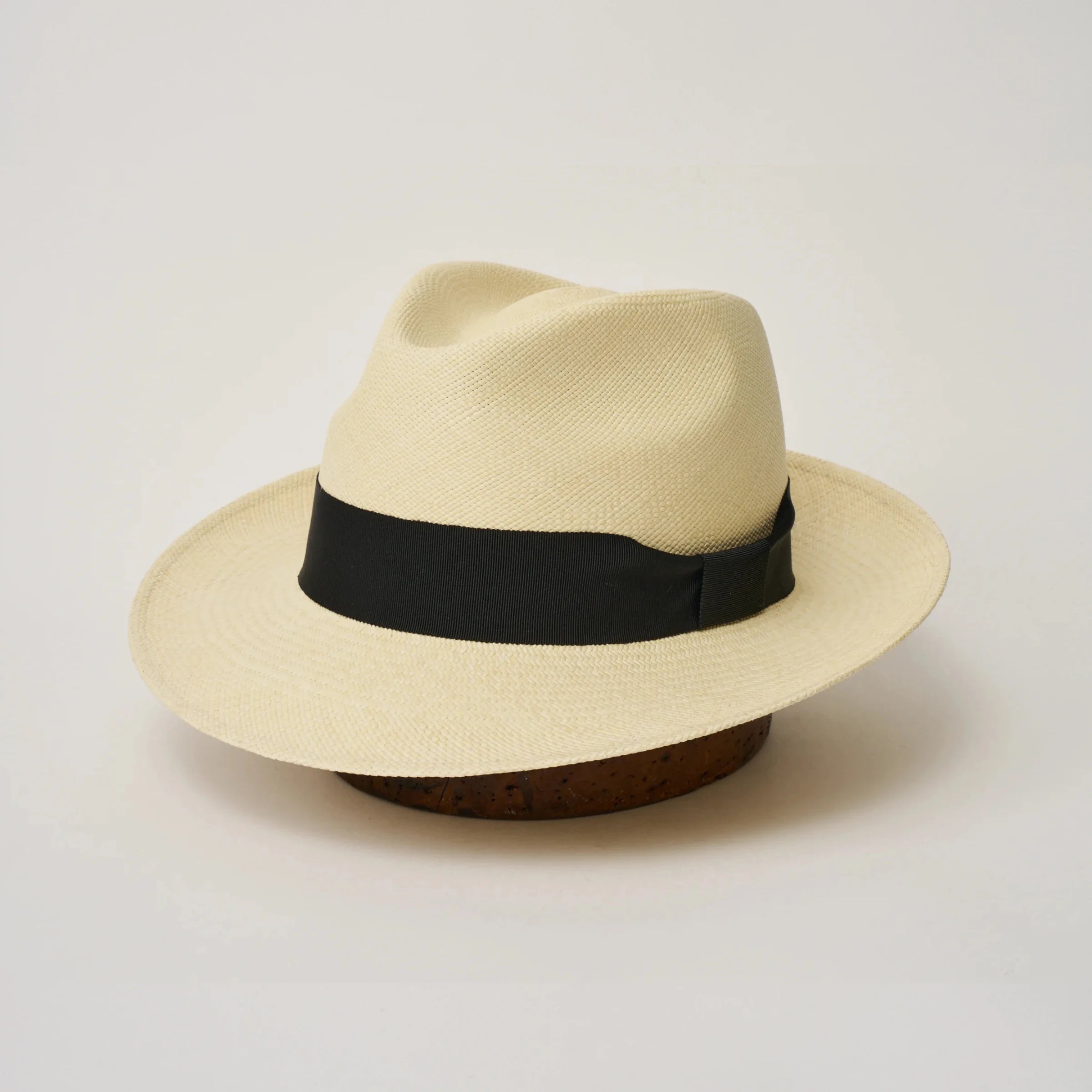 Studio image, three-quarter view of the Camilo New Fedora Fino Natural coloured Panama Hat with Black trim, showing the crown shape, front crease and ribbon trim.