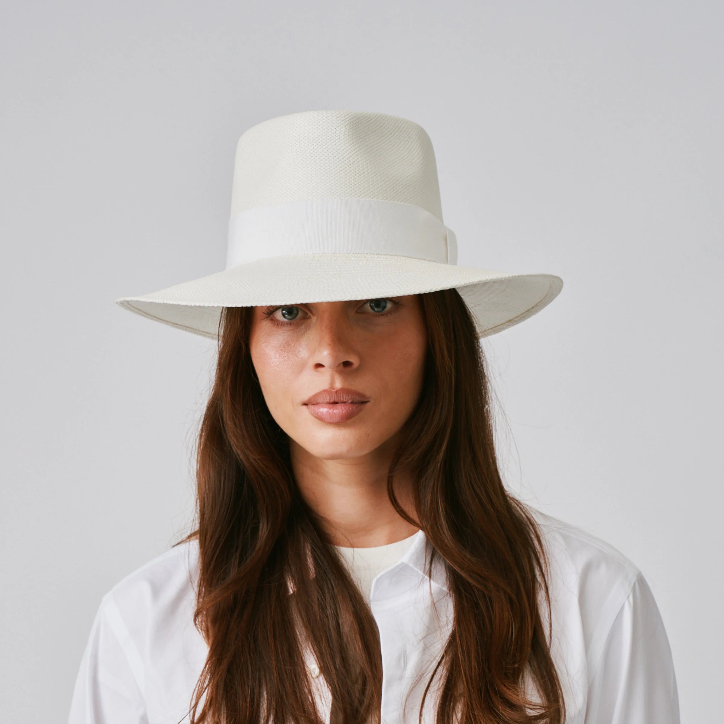 Woman wearing a Country Cream / White Panama hat and white tee against a plain background.