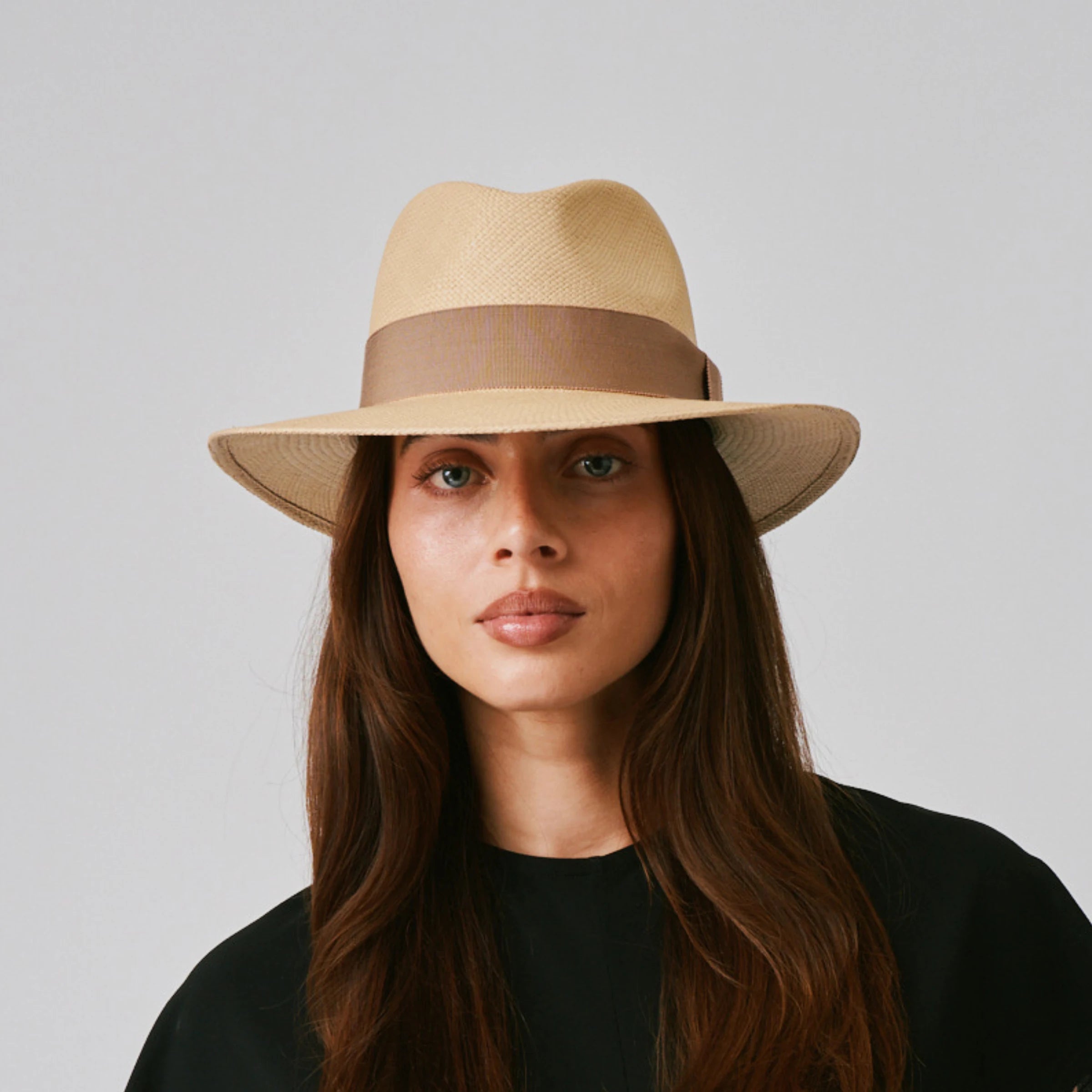 Woman wearing a Executive Sand / Oat Panama hat and black top against a plain background.