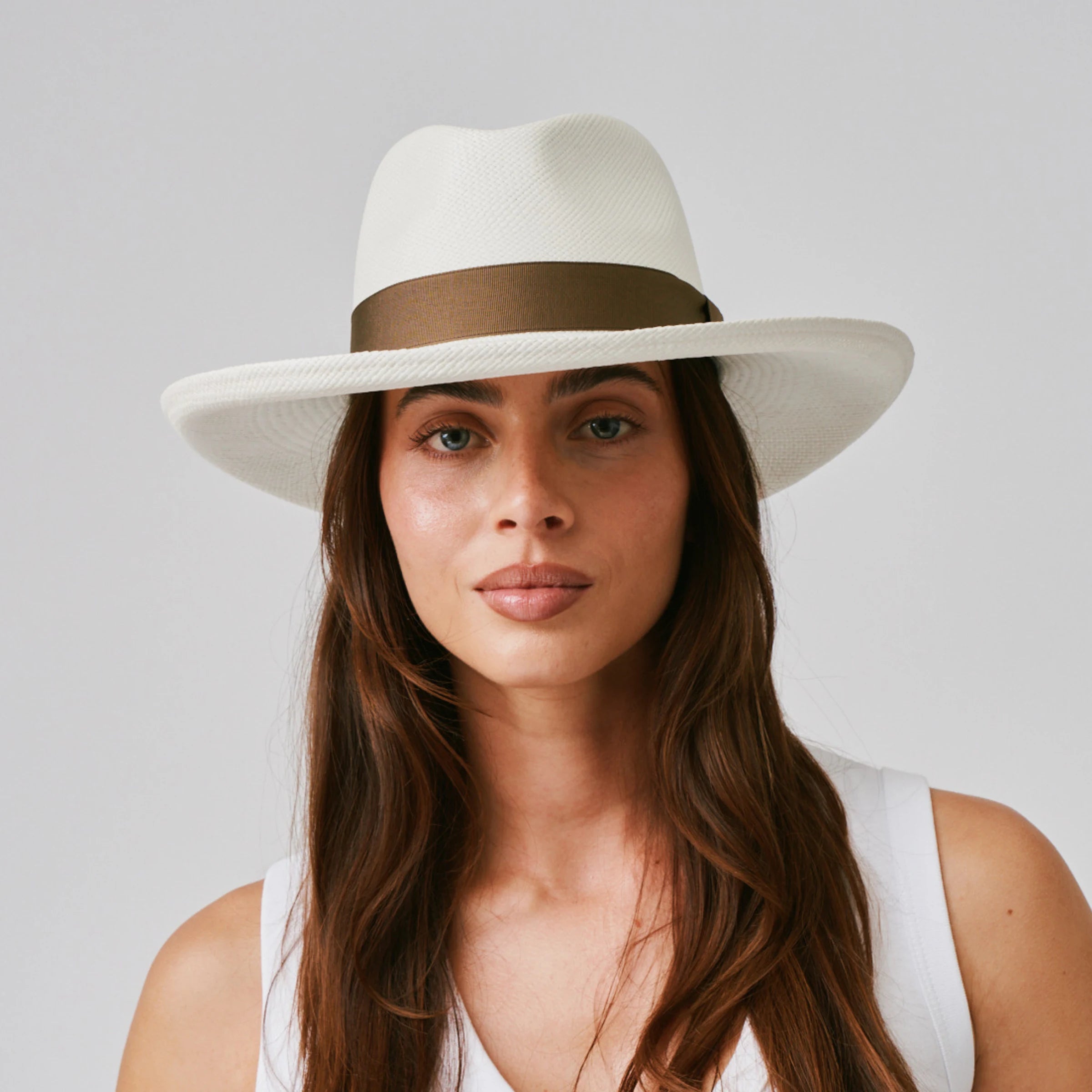 Woman wearing a Grand Planter Cream / Fawn Panama hat and white singlet against a plain background.