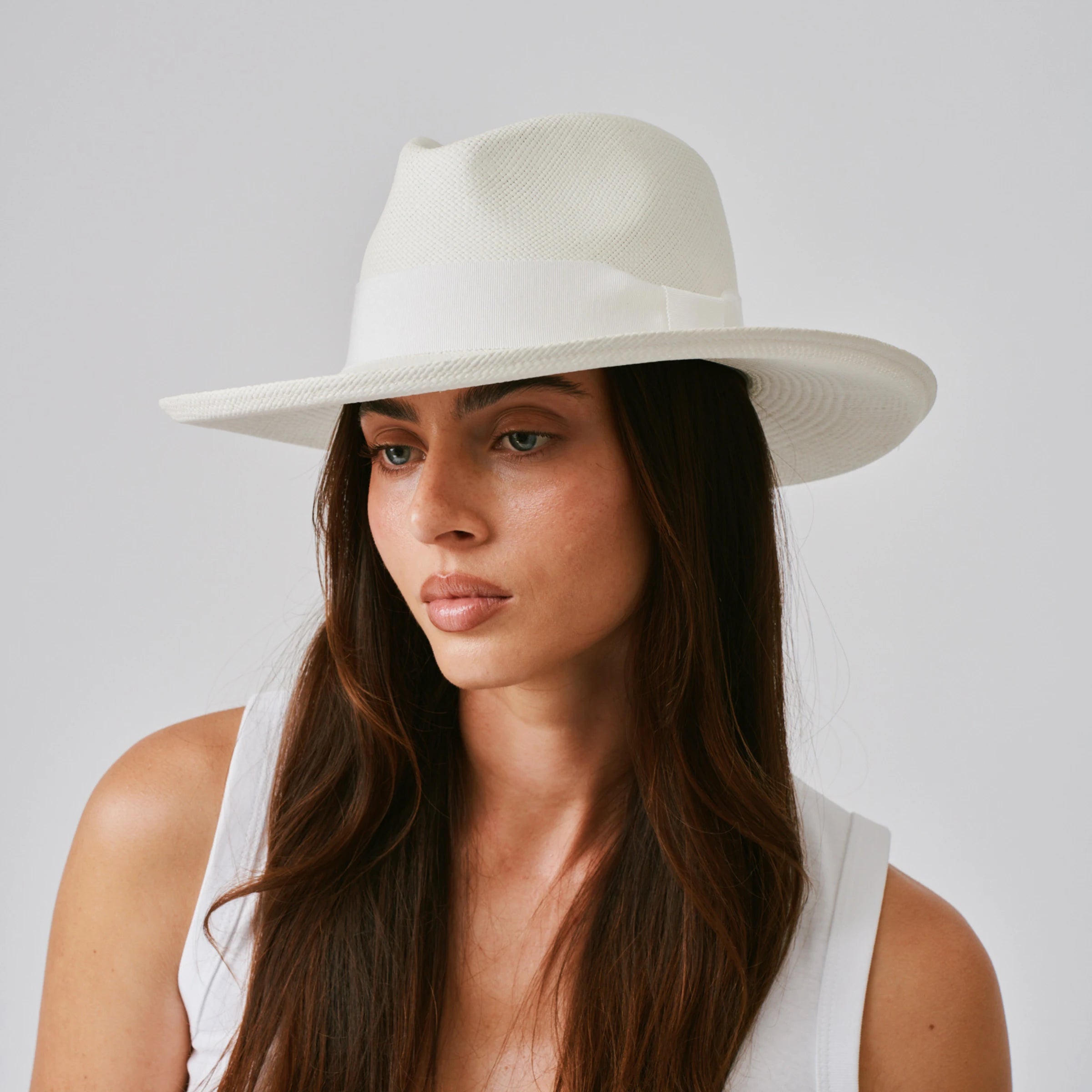 Woman wearing a Grand Planter Cream / White Panama hat against a plain background.