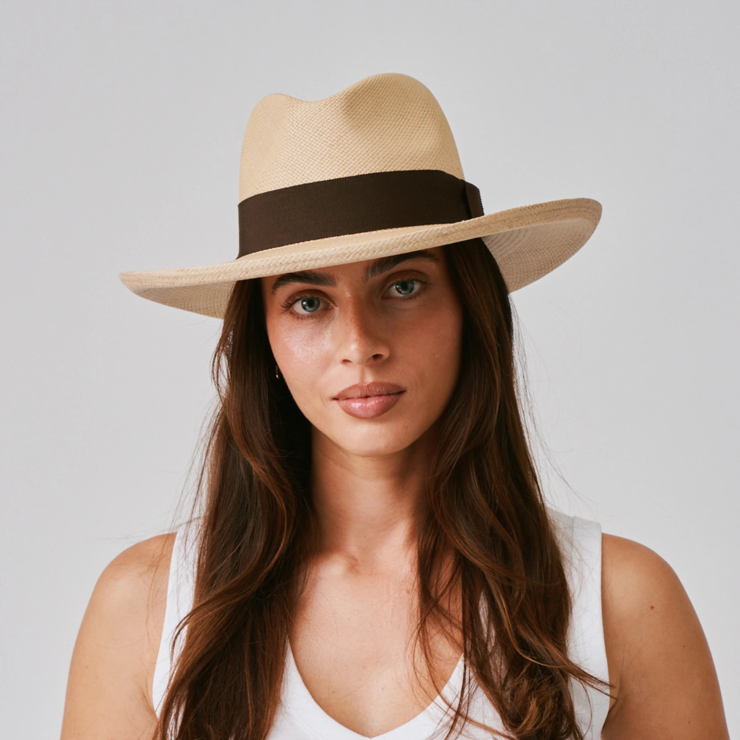 Woman wearing a Grand Planter Sand / Chocolate Panama hat and a white singlet against a plain background.