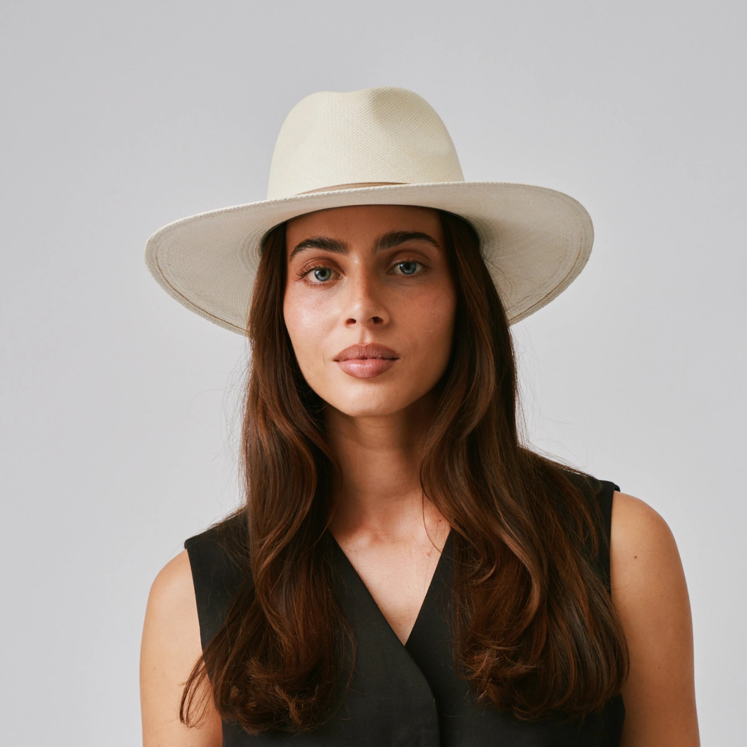 Woman wearing a Oro Natural / Taupe Panama hat and black top against a plain background.