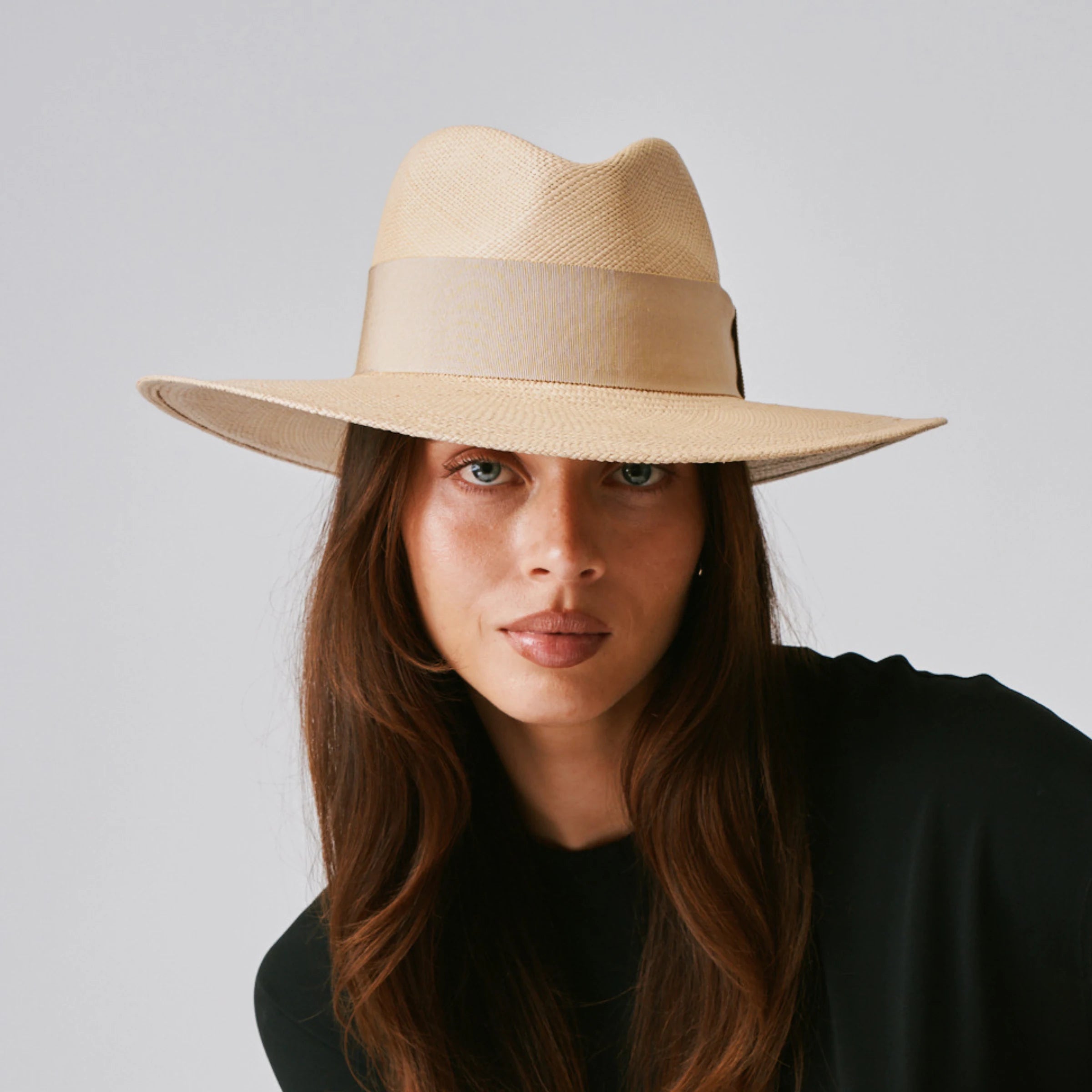 Woman wearing a Oro Sand / Camel Panama hat and black top against a plain background.