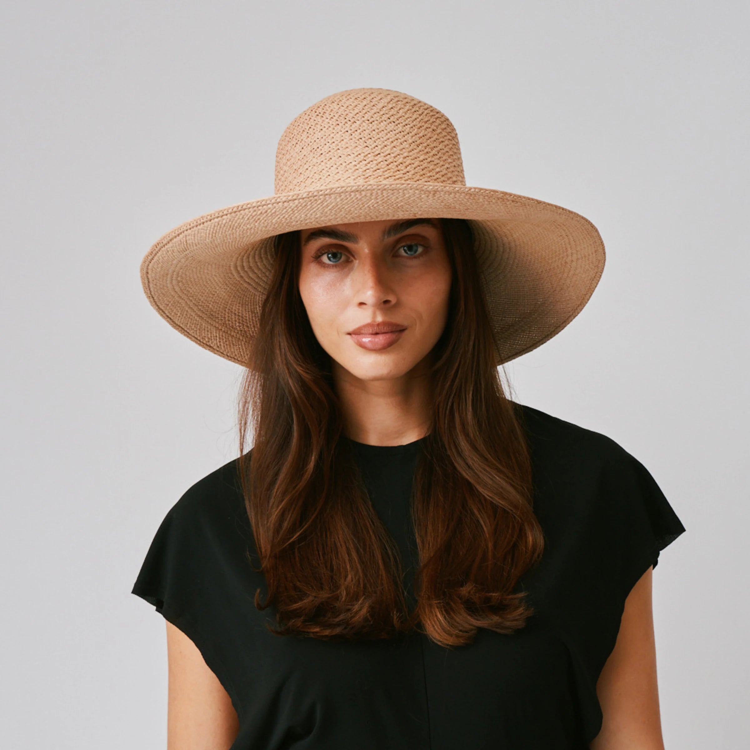 Woman wearing a Rio Sand Panama hat and black top against a plain background.