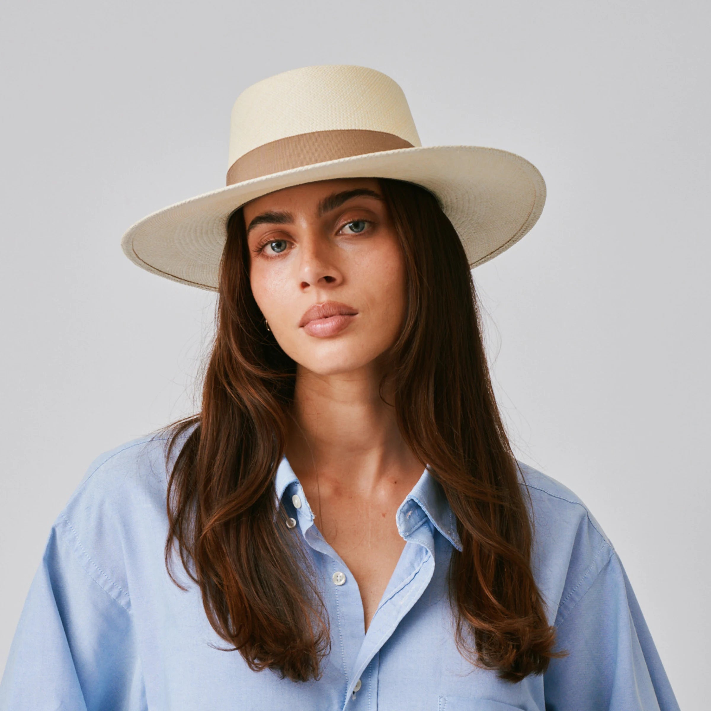 Woman wearing a Sol Natural / Oat Panama hat and blue shirt against a plain background.