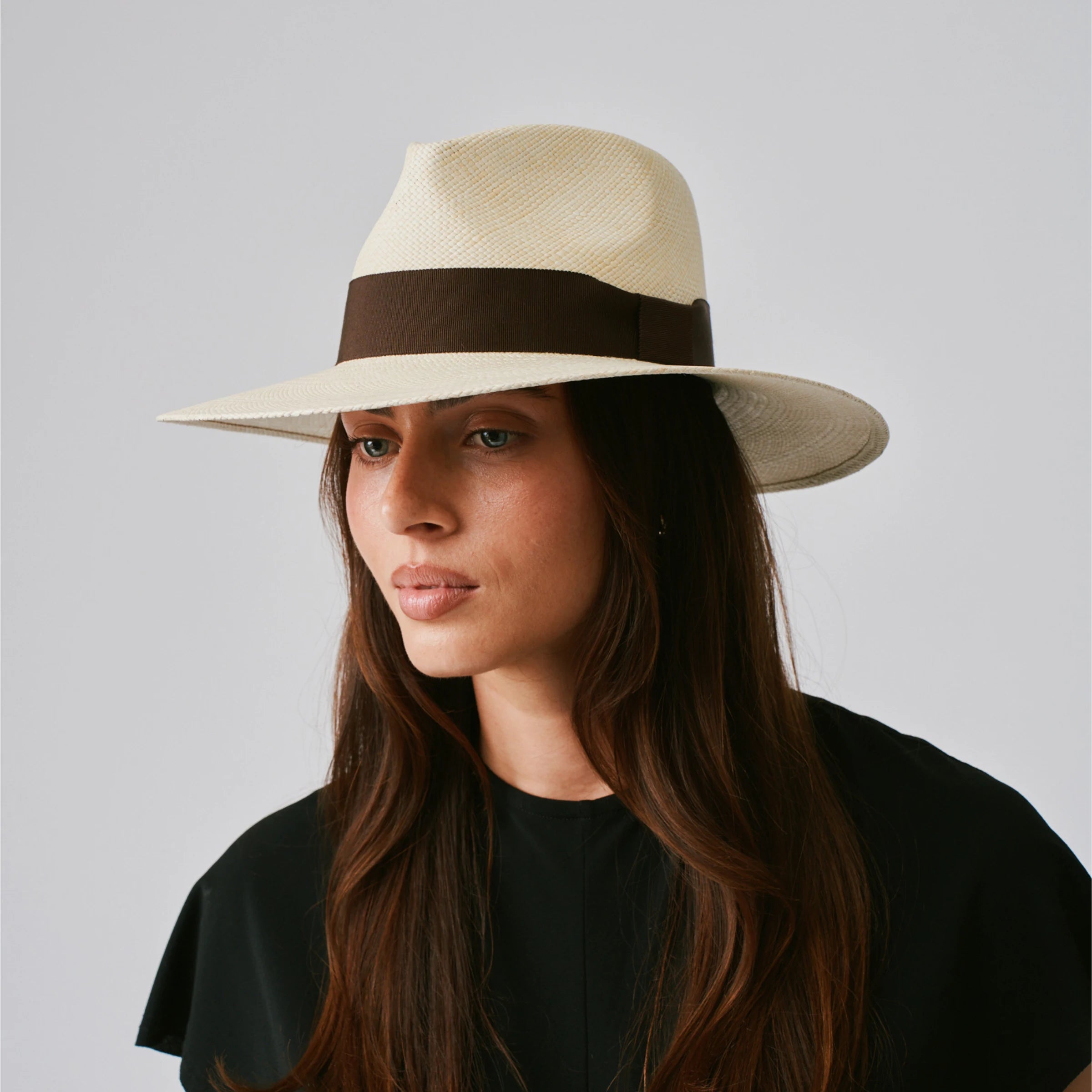 Woman wearing a Vita Natural / Chocolate Panama hat against a plain background.