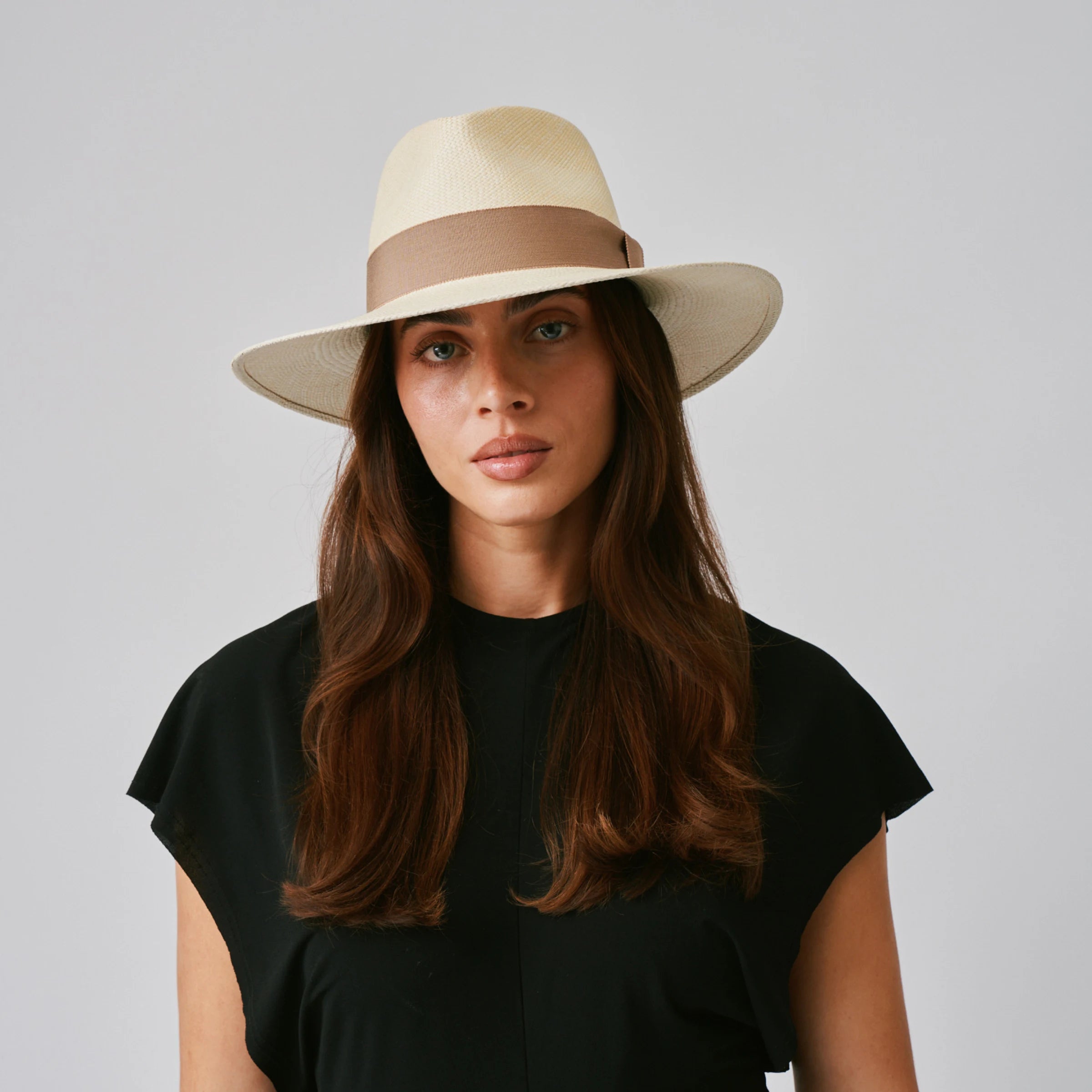 Woman wearing a Vita Natural / Oat Panama hat and black top against a plain background.