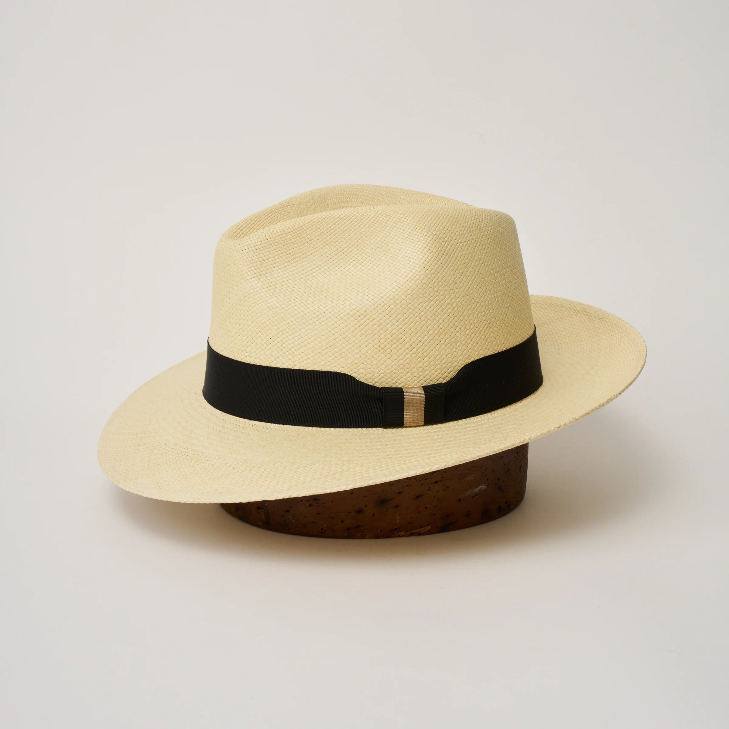 Studio image of the Camilo Classic Natural coloured Panama Hat with Black trim shown from the side, showing the brim shape and ribbon finish.