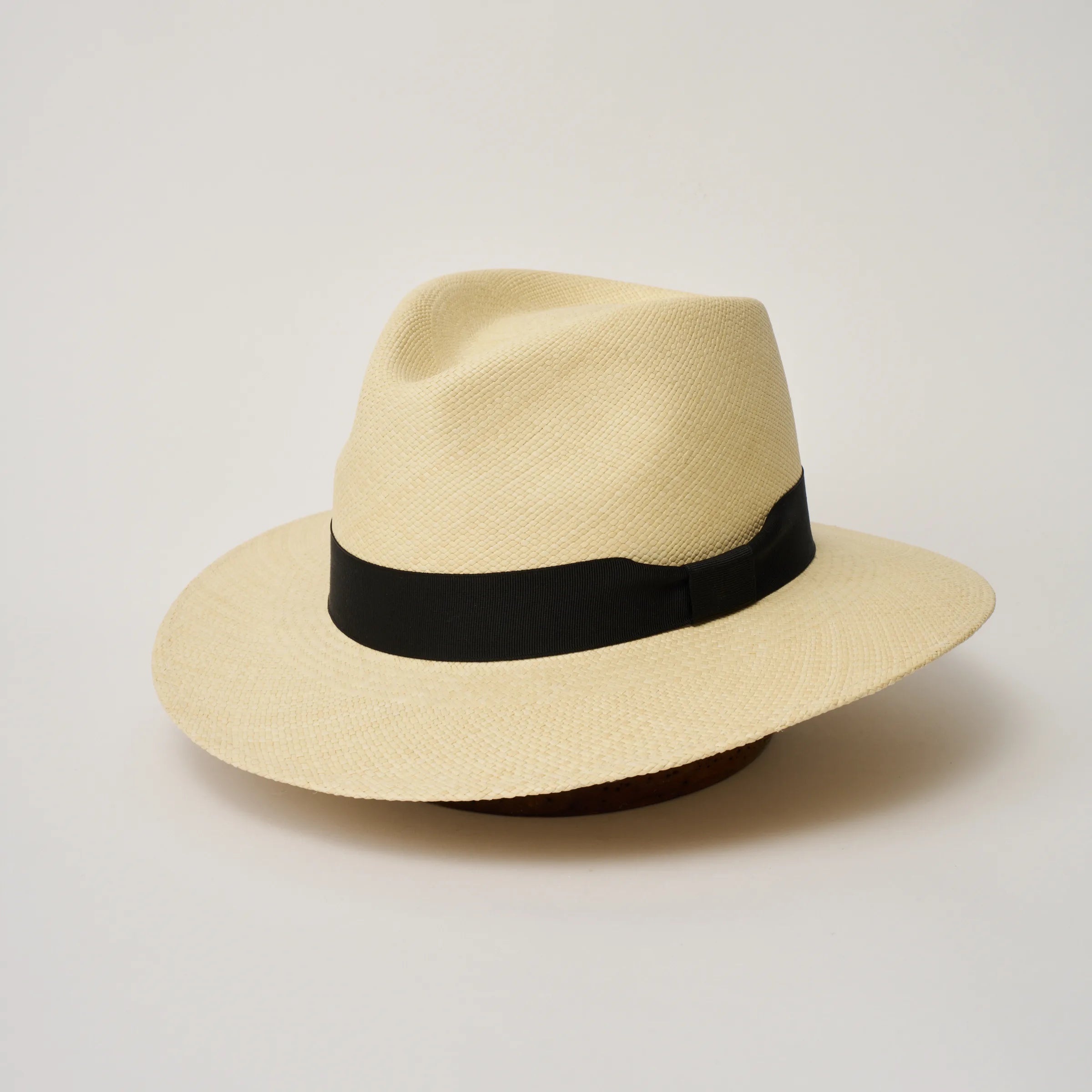 Studio image of the Camilo Executive Natural coloured Panama Hat with Black trim, angled showing the crown shape, front crease and ribbon details.