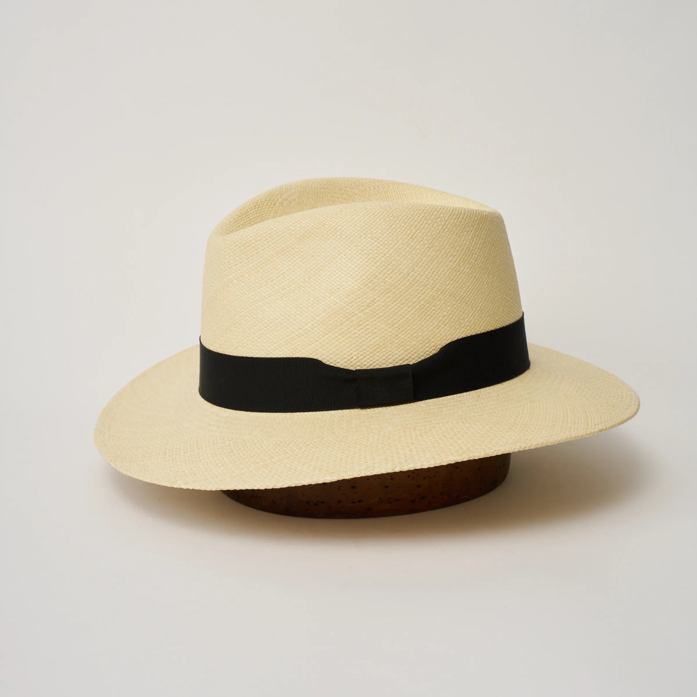 Studio image of the Camilo Executive 
Natural coloured Panama Hat with Black trim shown from the side, showing the brim shape and ribbon finish.
