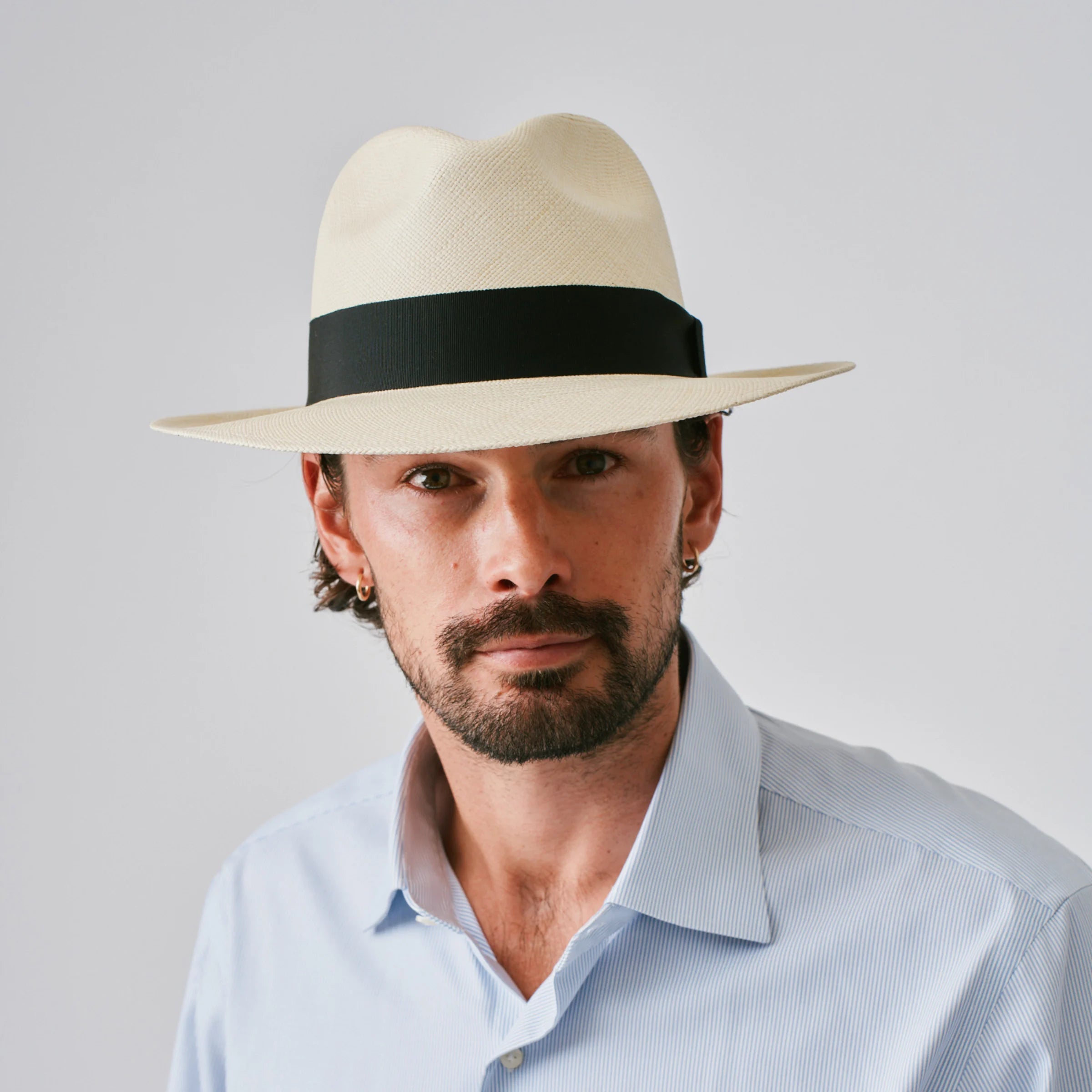 Man wearing a Camilo Classic Fino Natural / Black Panama hat and blue shirt against a plain background.
