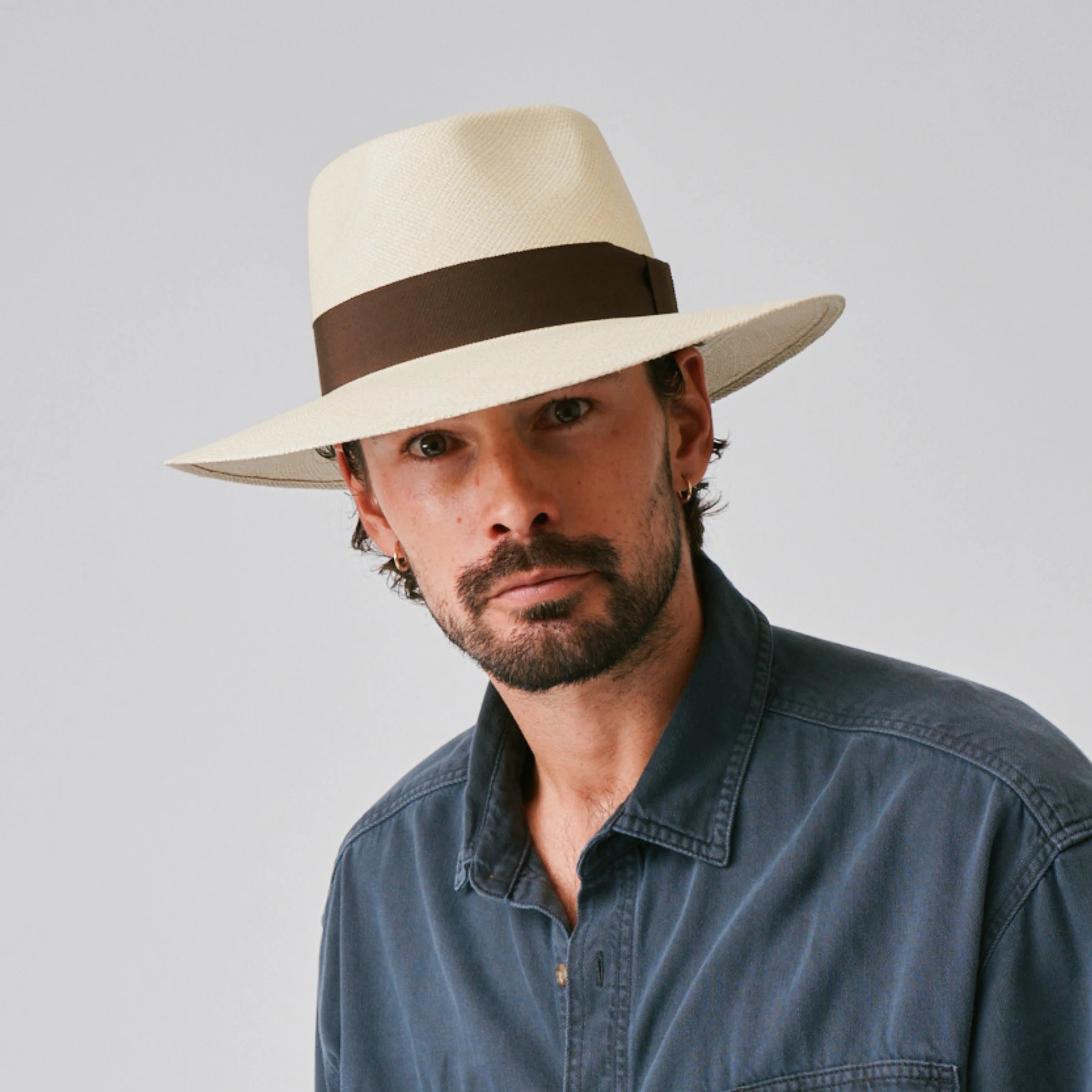 Man wearing a Country Natural / Chocolate Panama hat and blue shirt against a plain background.