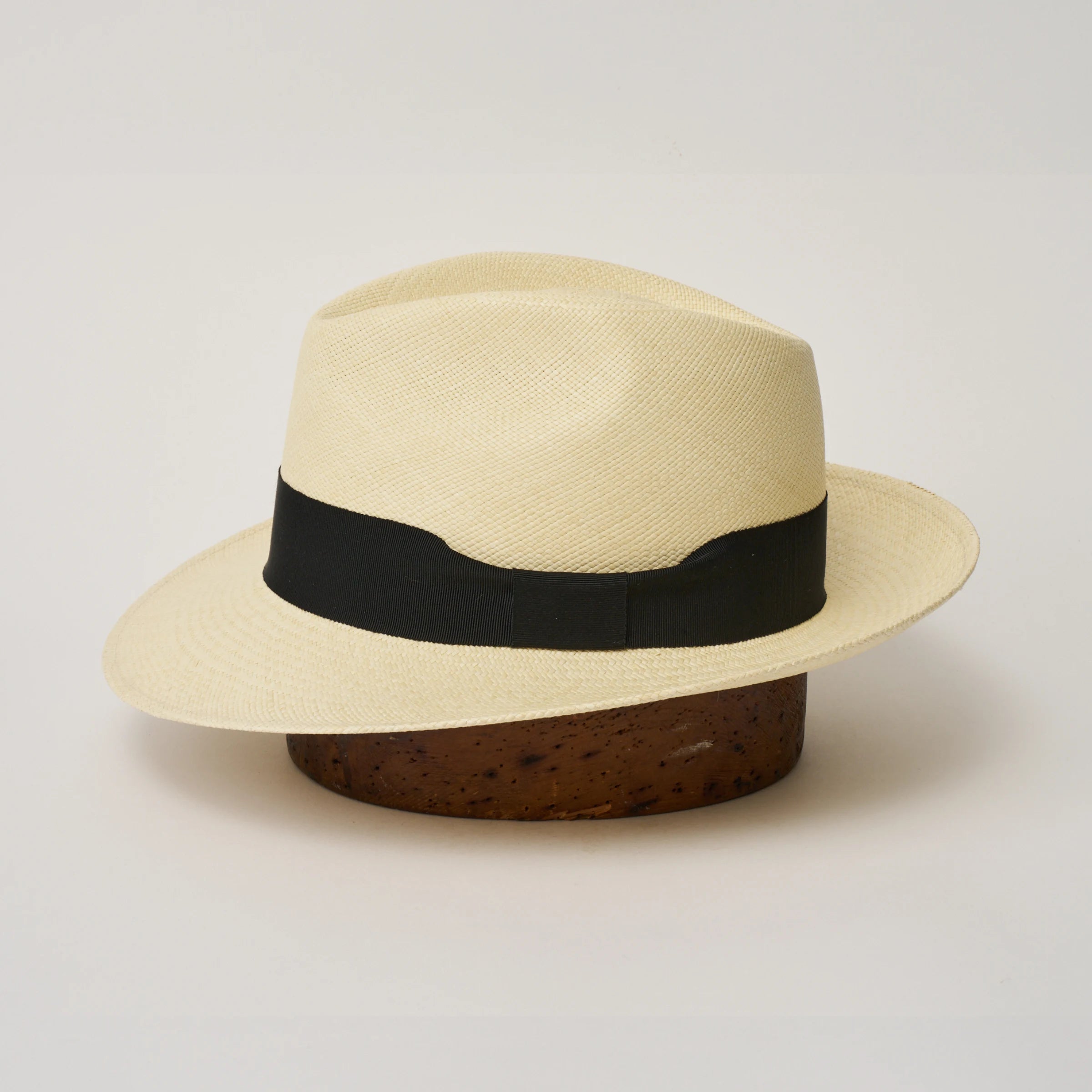 Studio image of the Camilo New Fedora Fino Natural coloured Panama Hat with Black trim shown from the side, showing the brim shape and ribbon finish.