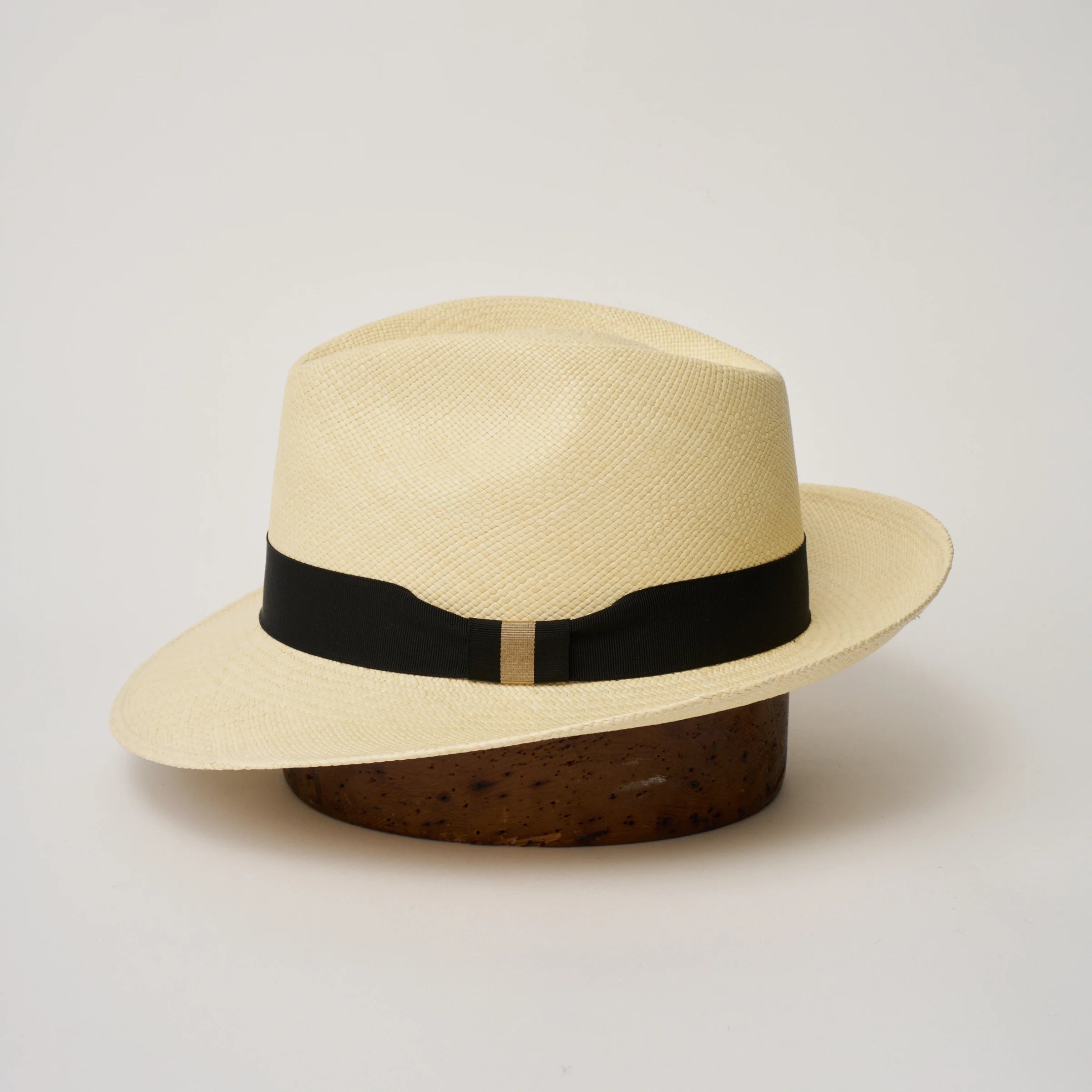 Studio image of the Camilo New Fedora Natural coloured Panama Hat with Black trim shown from the side, showing the brim shape and ribbon finish.