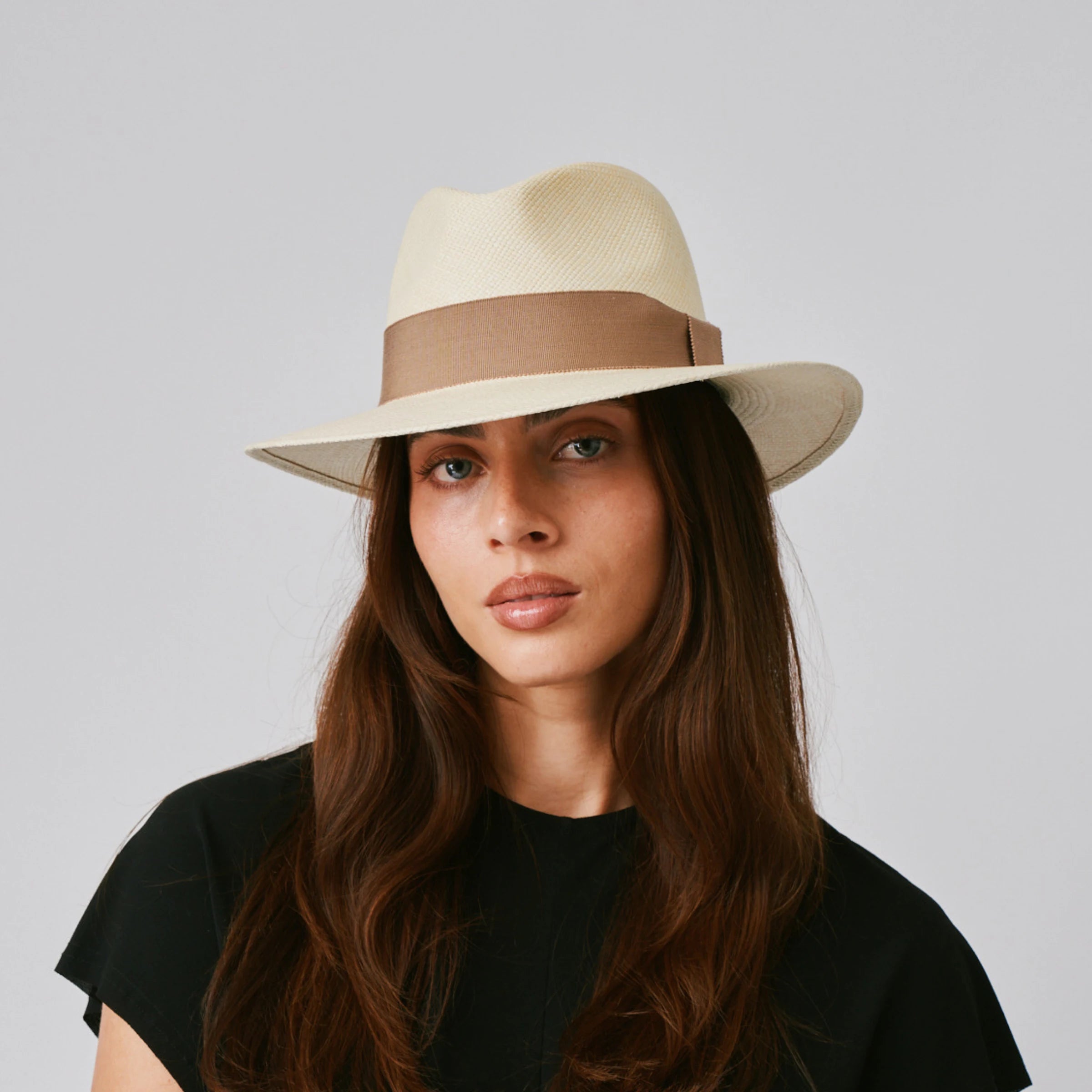 Woman wearing a Executive Natural / Oat Panama hat and black top against a plain background.