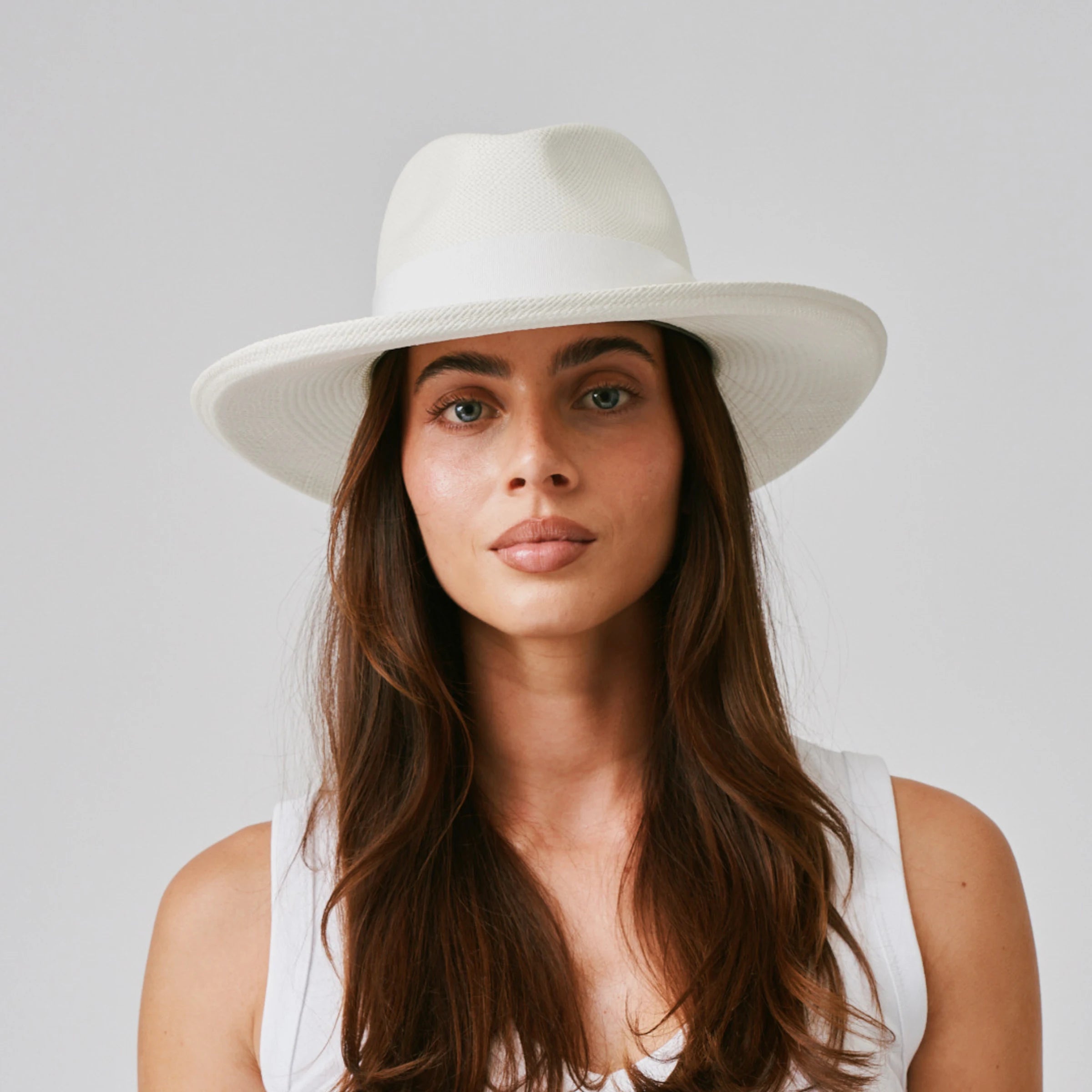 Woman wearing a Grand Planter Cream / White  Panama hat and white singlet against a plain background.