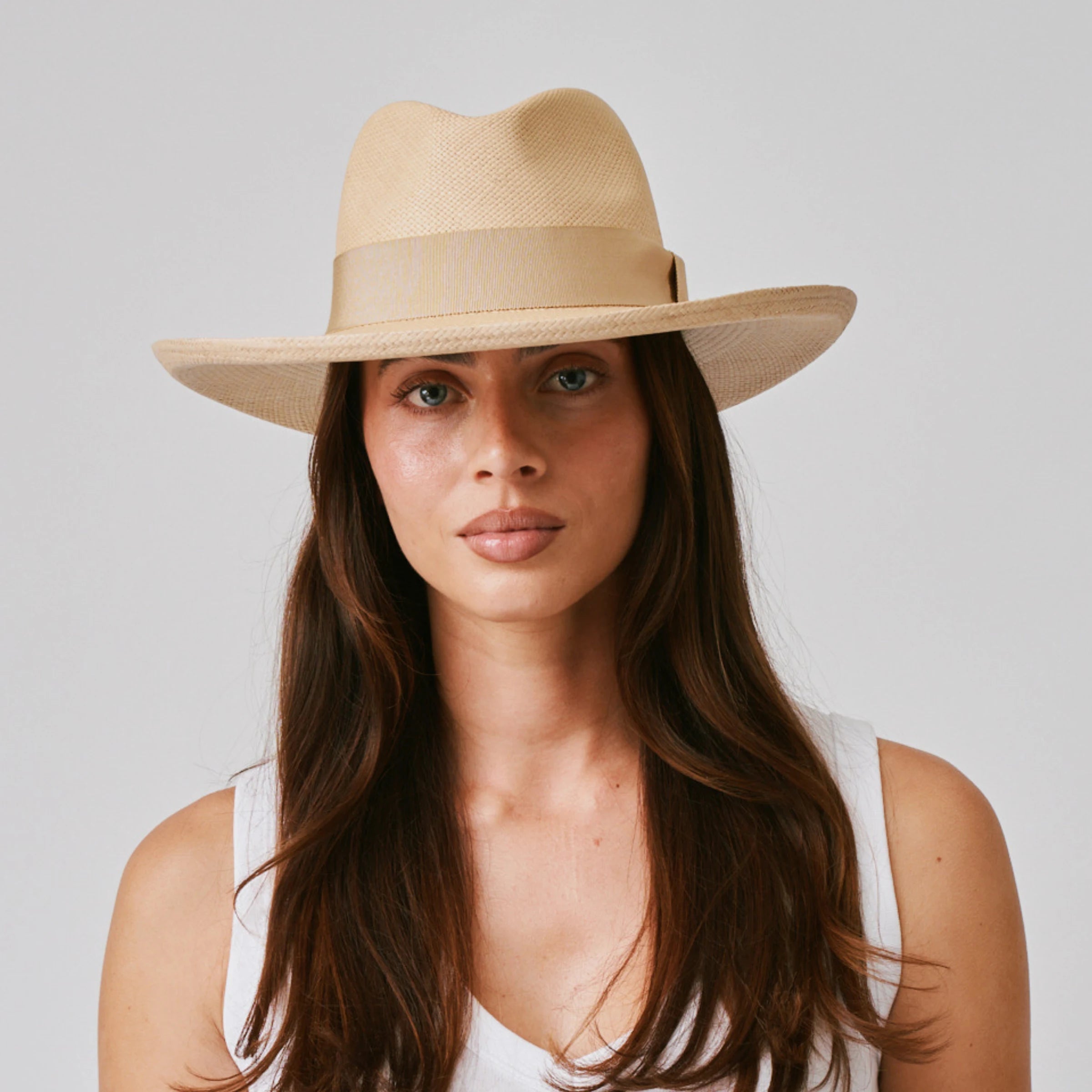 Woman wearing a Grand Planter Sand / Camel Panama hat and white singlet against a plain background.