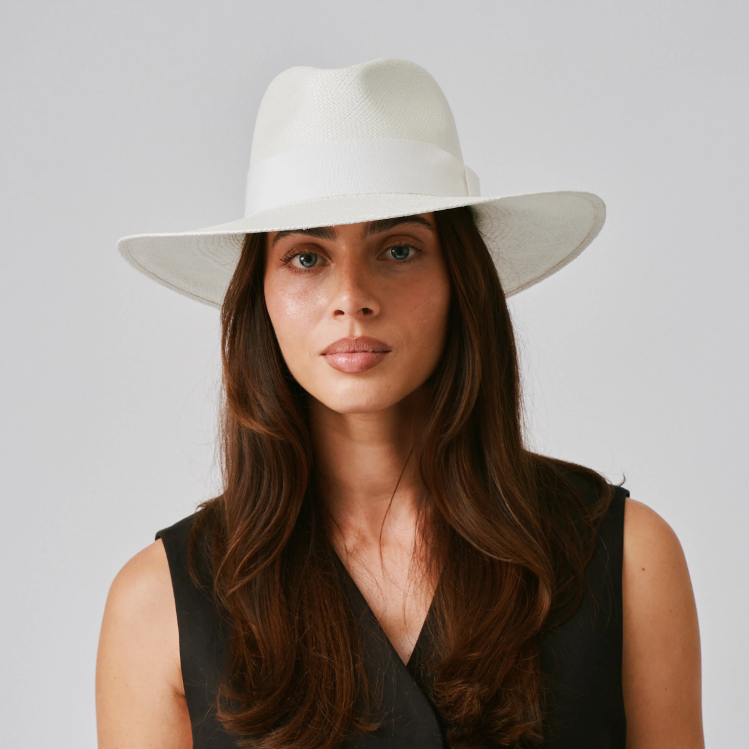 Woman wearing a Oro Cream / White Panama hat and black top against a plain background.