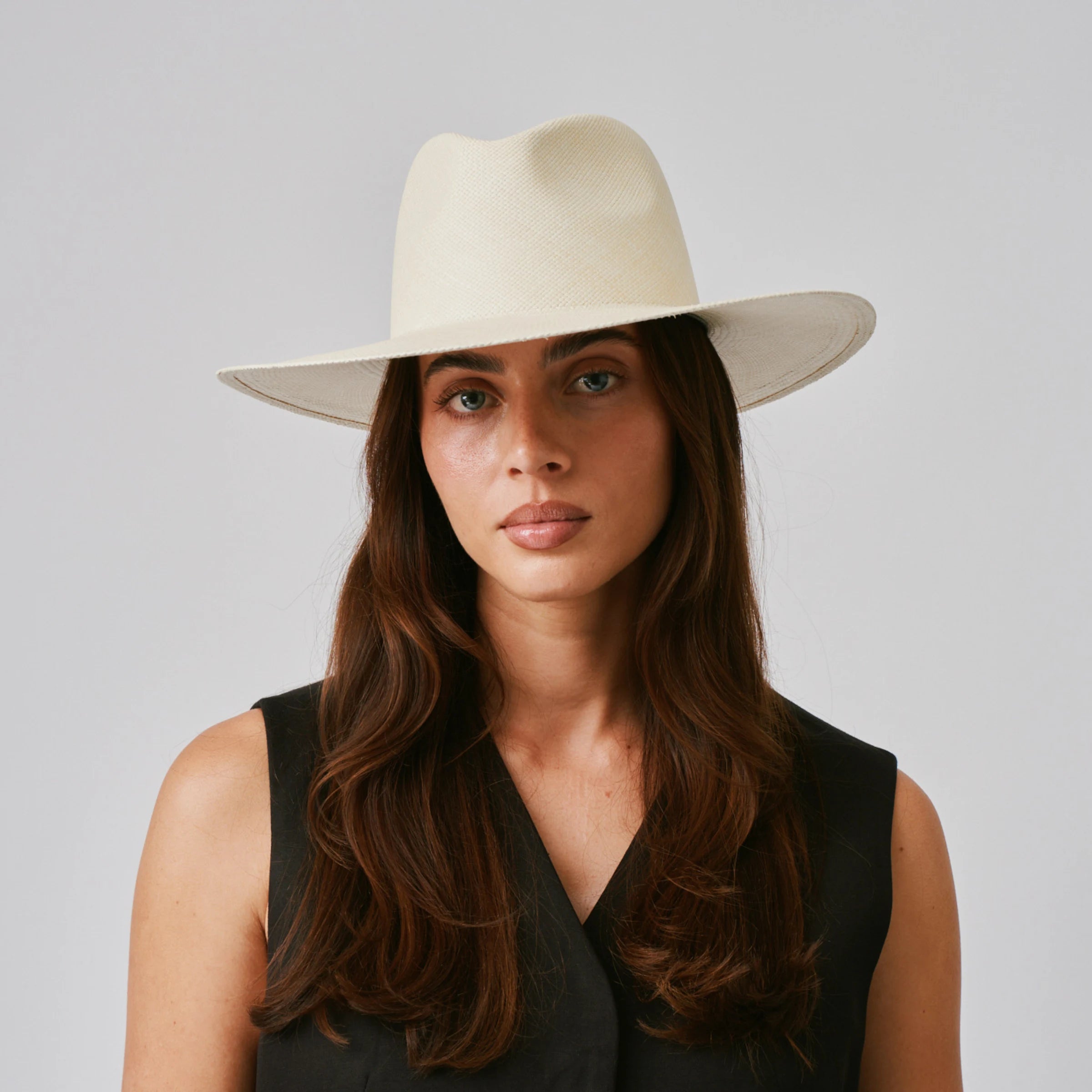 Woman wearing a Oro Natural Panama hat and black top against a plain background.