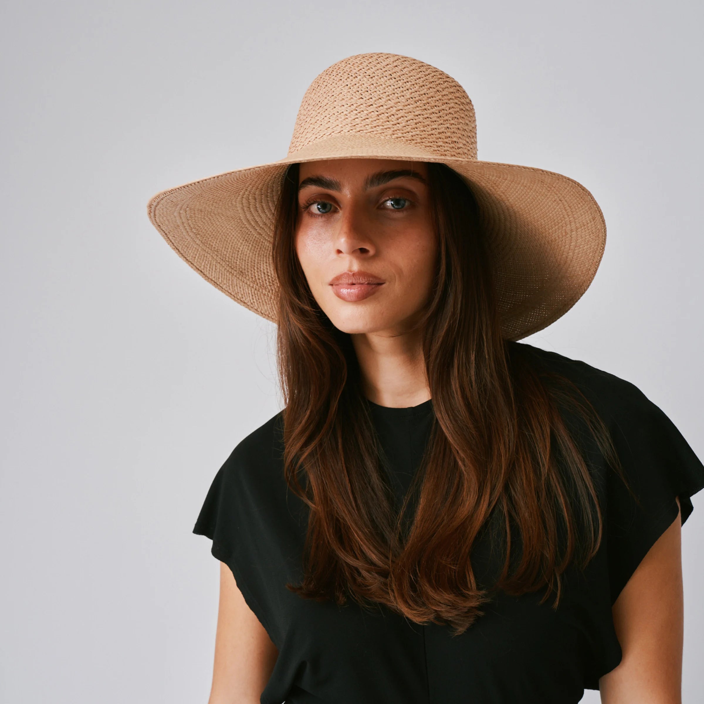 Woman wearing a Rio Sand Panama hat and black top against a plain background.