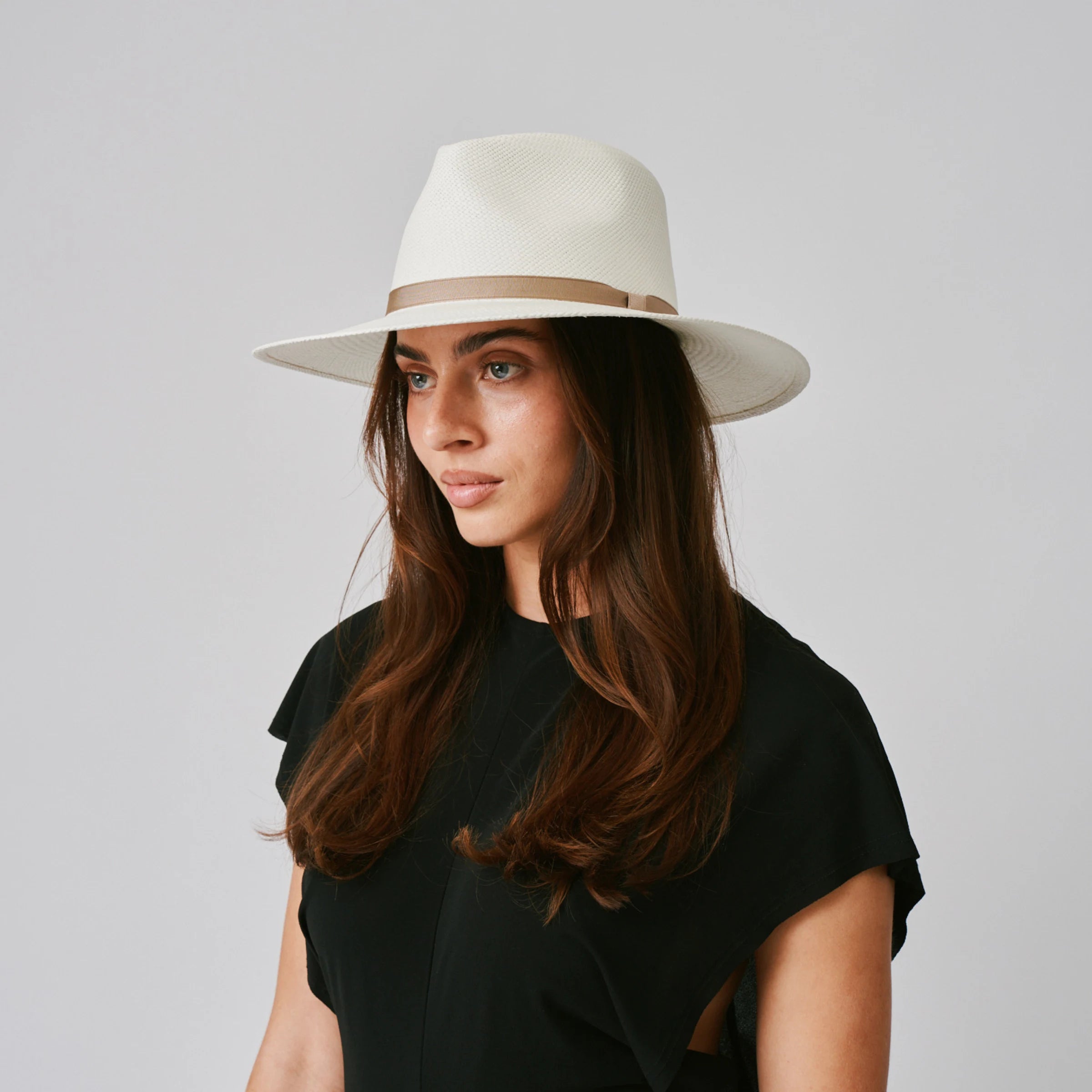 Woman wearing a Vita Cream / Tan  Panama hat and black top against a plain background.