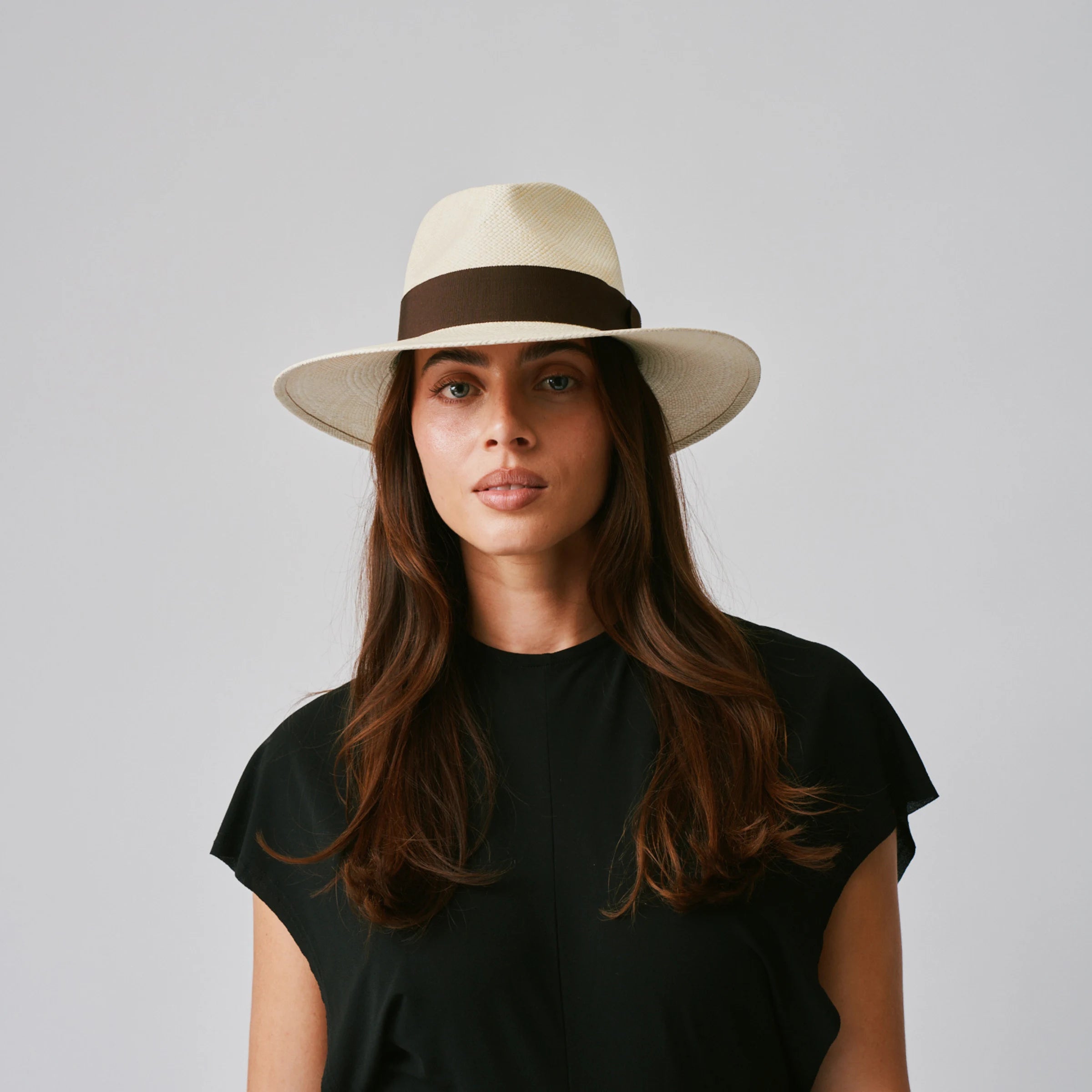 Woman wearing a Vita Natural / Chocolate Panama hat and black top against a plain background.