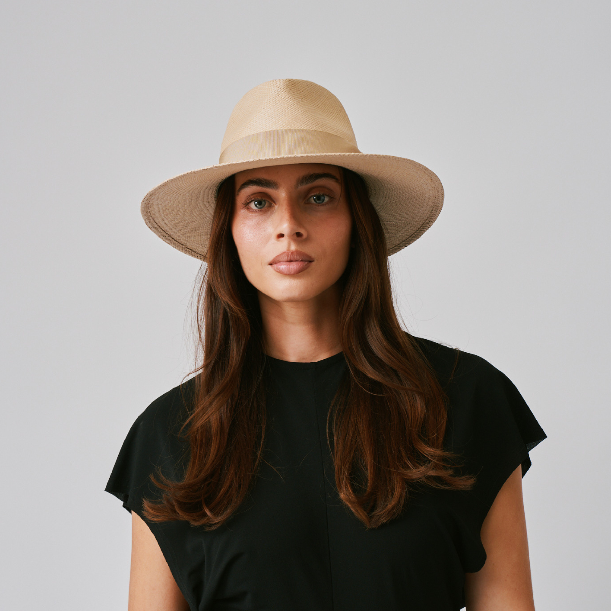 Woman wearing a Vita Sand / Camel Panama hat and black top against a plain background.